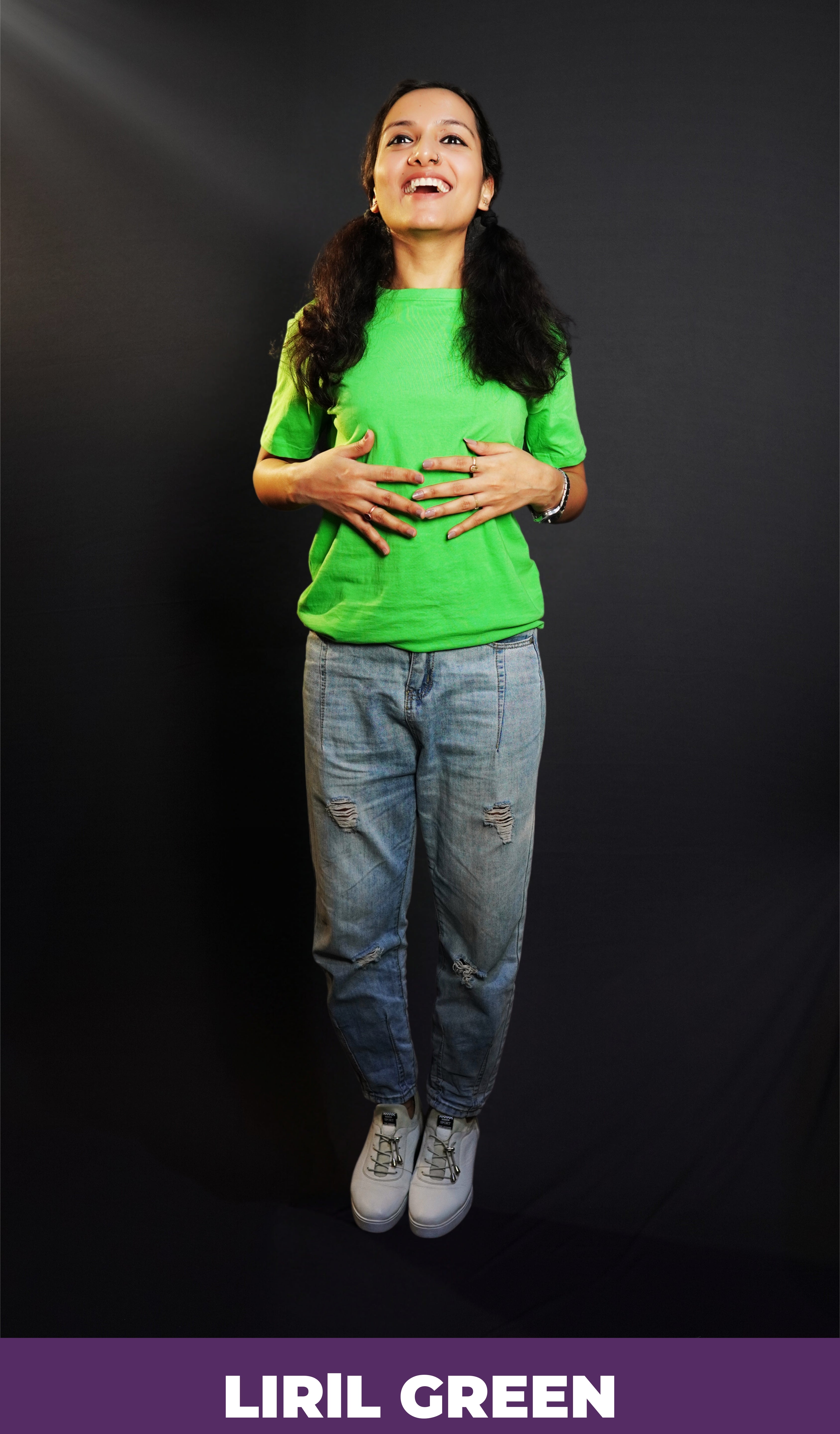 A woman laughing happily standing against a dark background as her hands gently lie on her stomach, wearing a liril green plain unisex round neck short sleeves t-shirt, showcasing a casual everyday look-Muselot