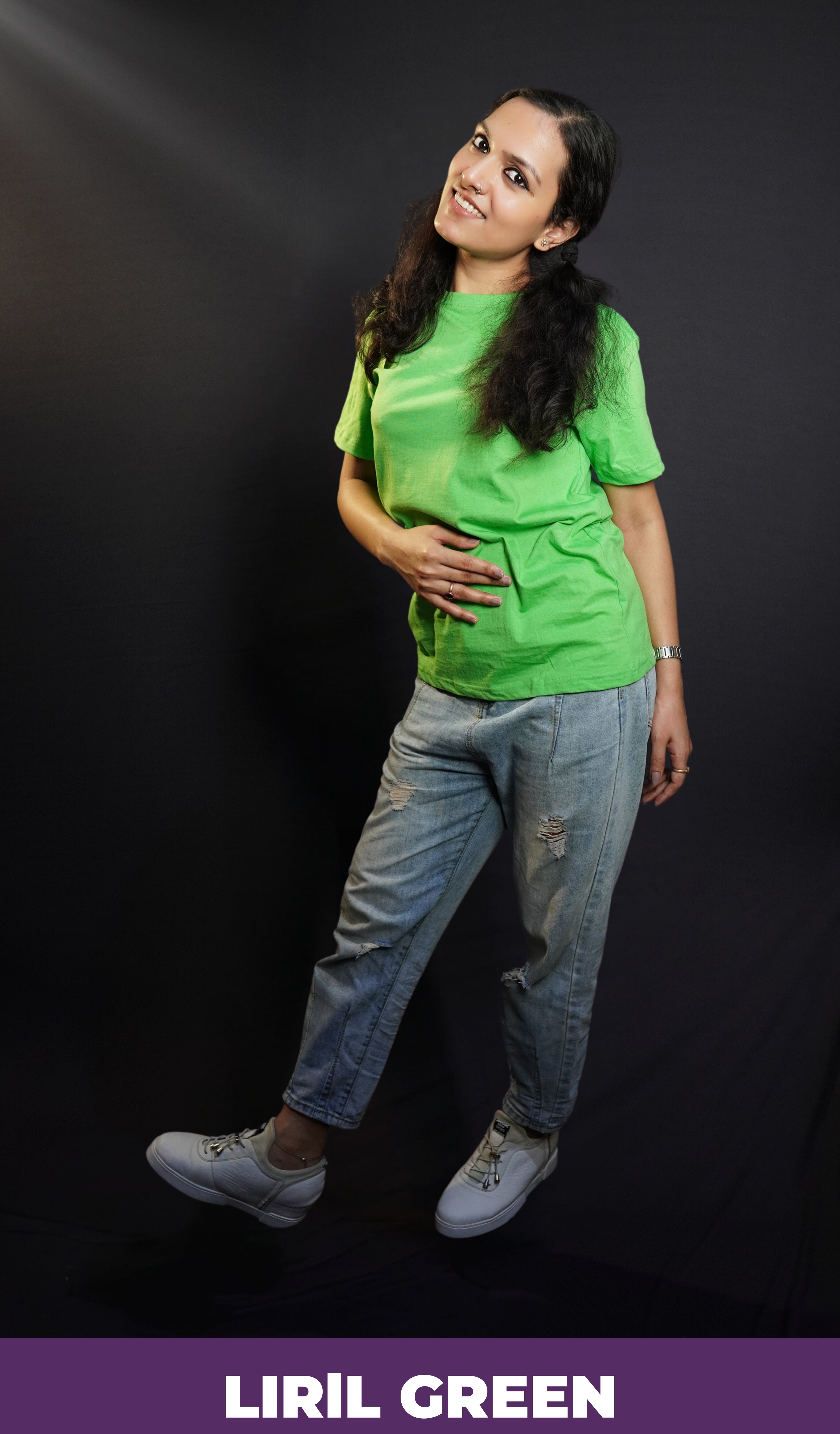 A woman in a long length unisex plain cotton liril green t-shirt, posing with her hand on her stomach and another behind her as she stands sideways, highlighting a modern comfortable fit-Muselot