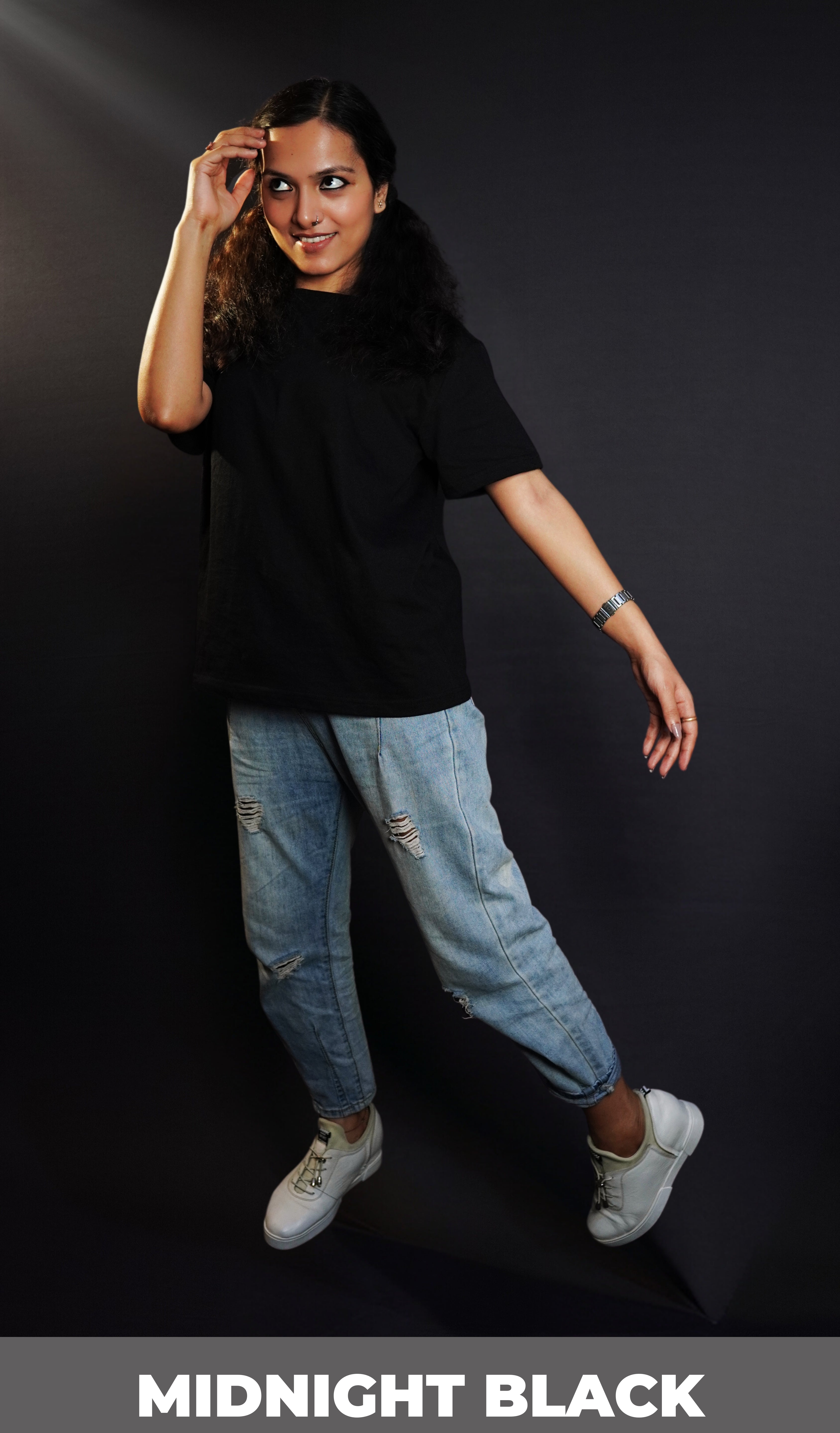 A woman posing with her hand barely touching her forehead as she sways at her side, wearing a round neck short sleeved stretchable moisture wicking midnight black t-shirt, highlighting a modern easygoing fit-Muselot
