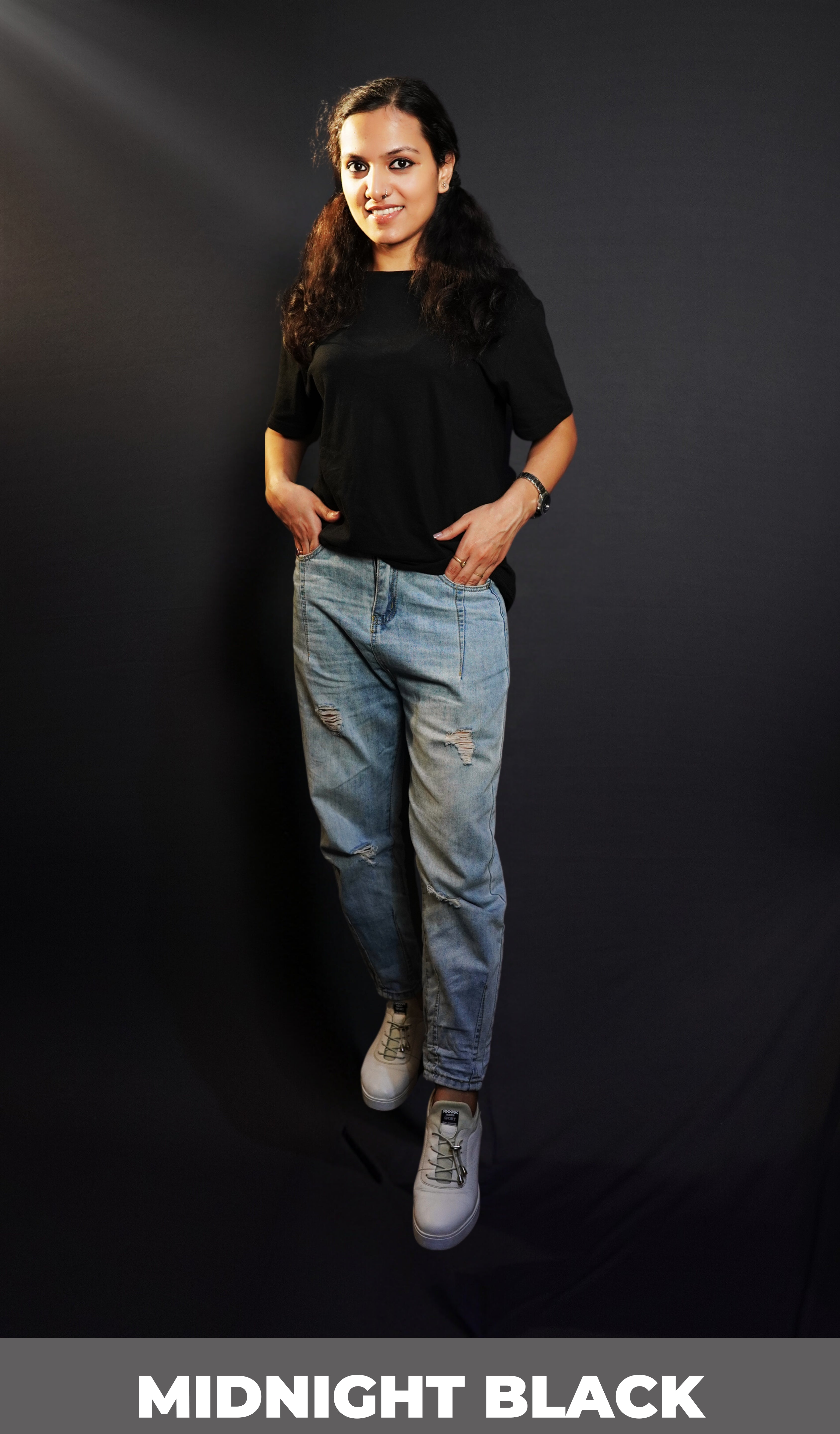 A model wearing a round neck cotton moisture wicking long length midnight black t-shirt, posing as her hands are slightly inside her jeans pockets, showcasing a classy trendy fit-Muselot
