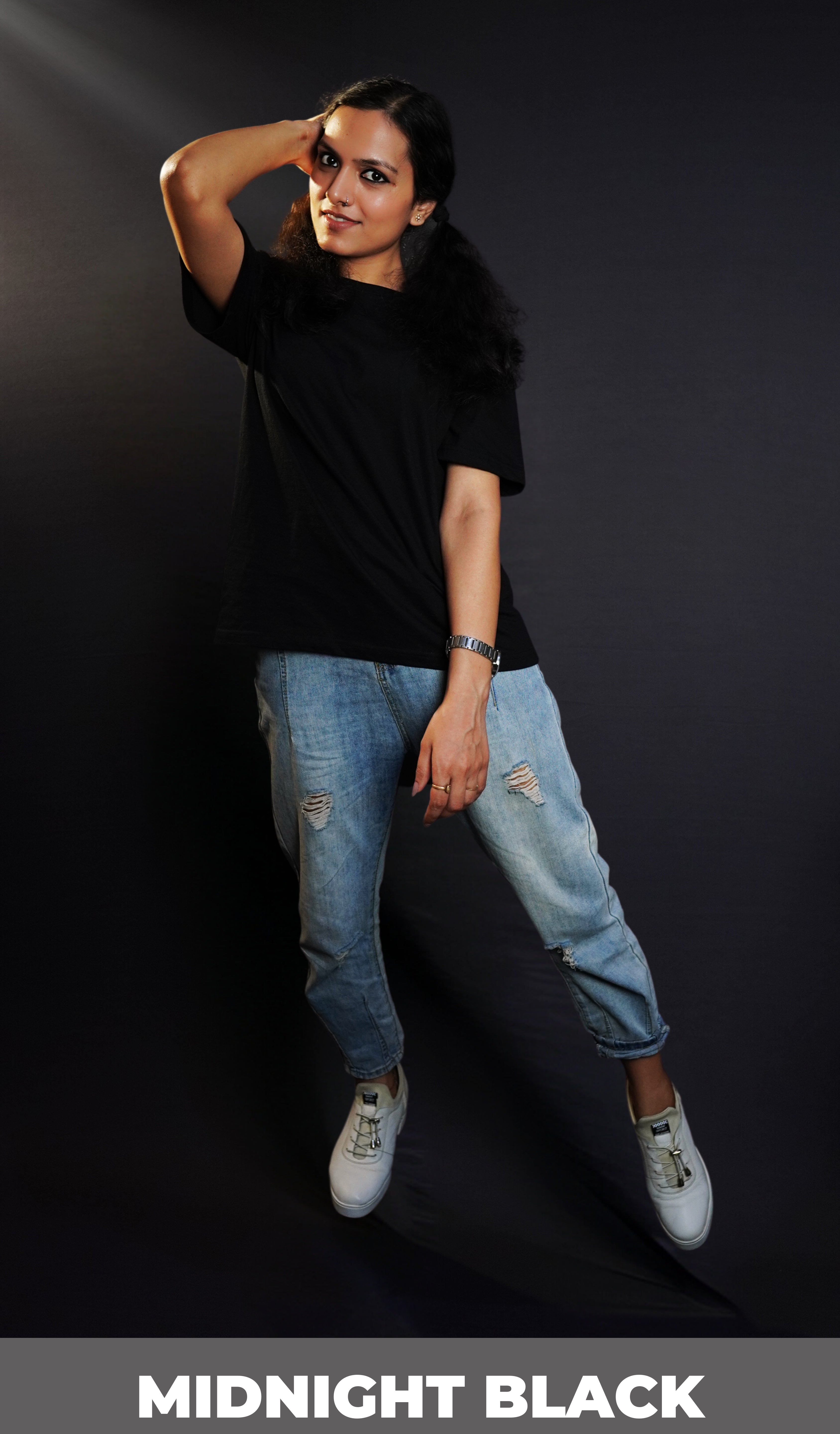 A stylish model wearing a plain short sleeved girl's cotton stretchable midnight black t-shirt, posing with her hand on the side of her head with elbow towards the camera, showcasing a fashionable snug fit-Muselot