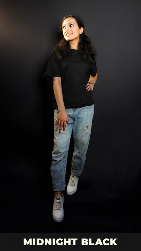 An elegant model wearing a short sleeved long length plain midnight black women's t-shirt, looking sideways as her hand gently lies on her waist and thigh, highlighting a stylish modern look-Muselot