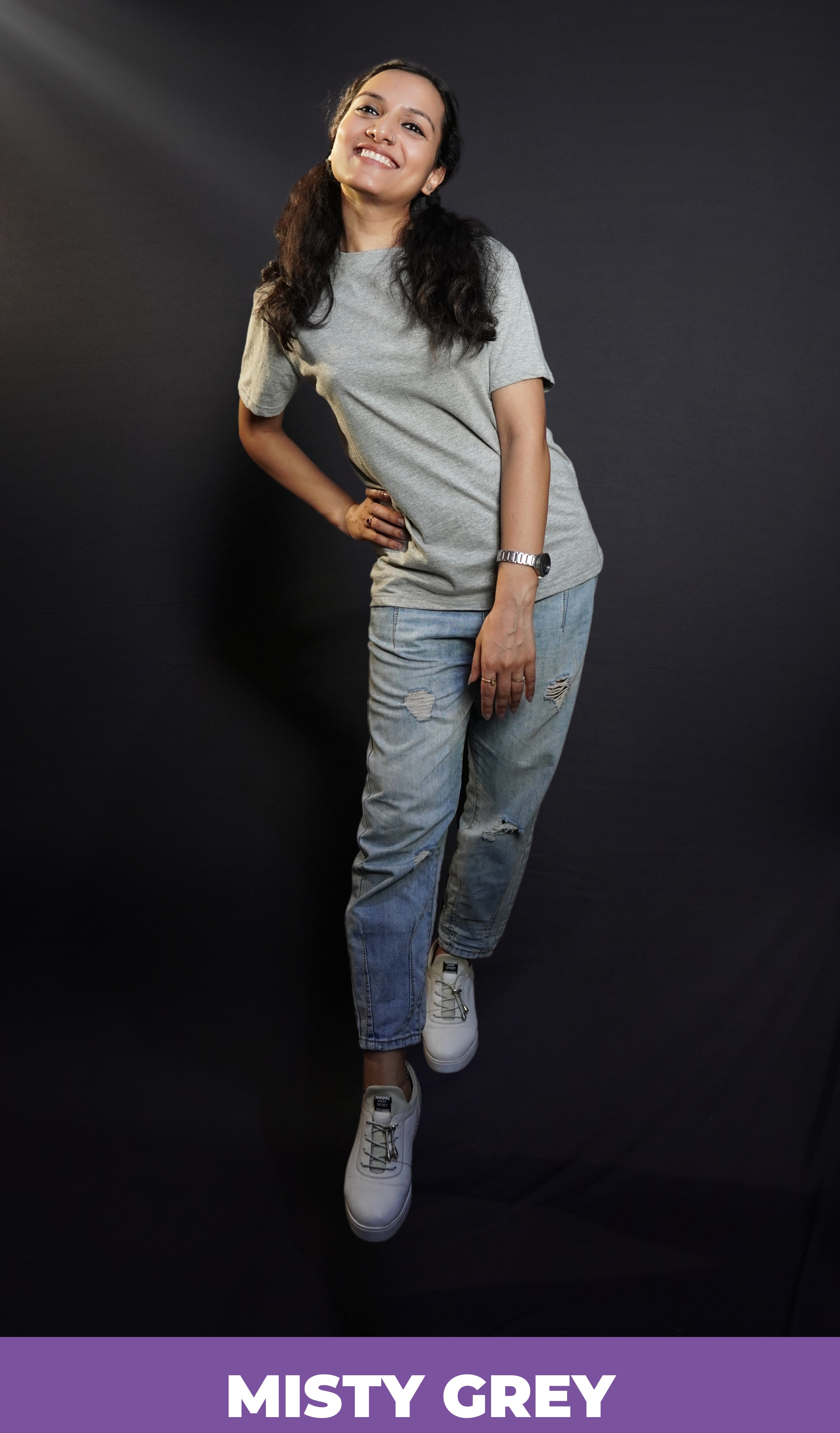 A cute woman wearing adult's round neck long length short sleeved misty grey t-shirt, posing with her hand on her waist as she sways to her side, highlighting a up to the minute easygoing fit-Muselot
