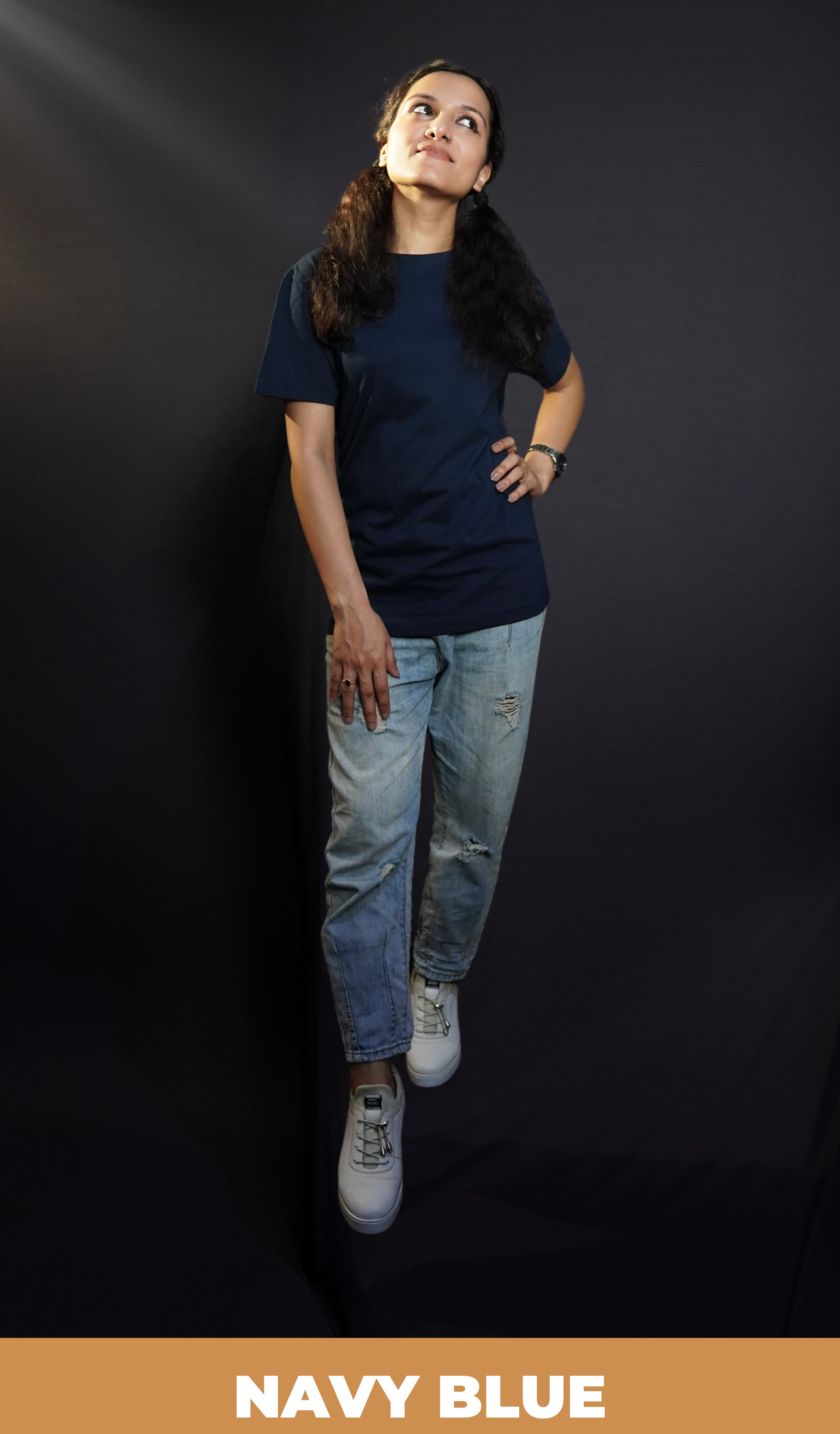 An elegant model wearing a women's cotton round neck stretchable plain navy blue t-shirt, posing with her hand on her waist and other on her thigh as she looks sideways with her chin up high, showcasing a popular modish look-Muselot