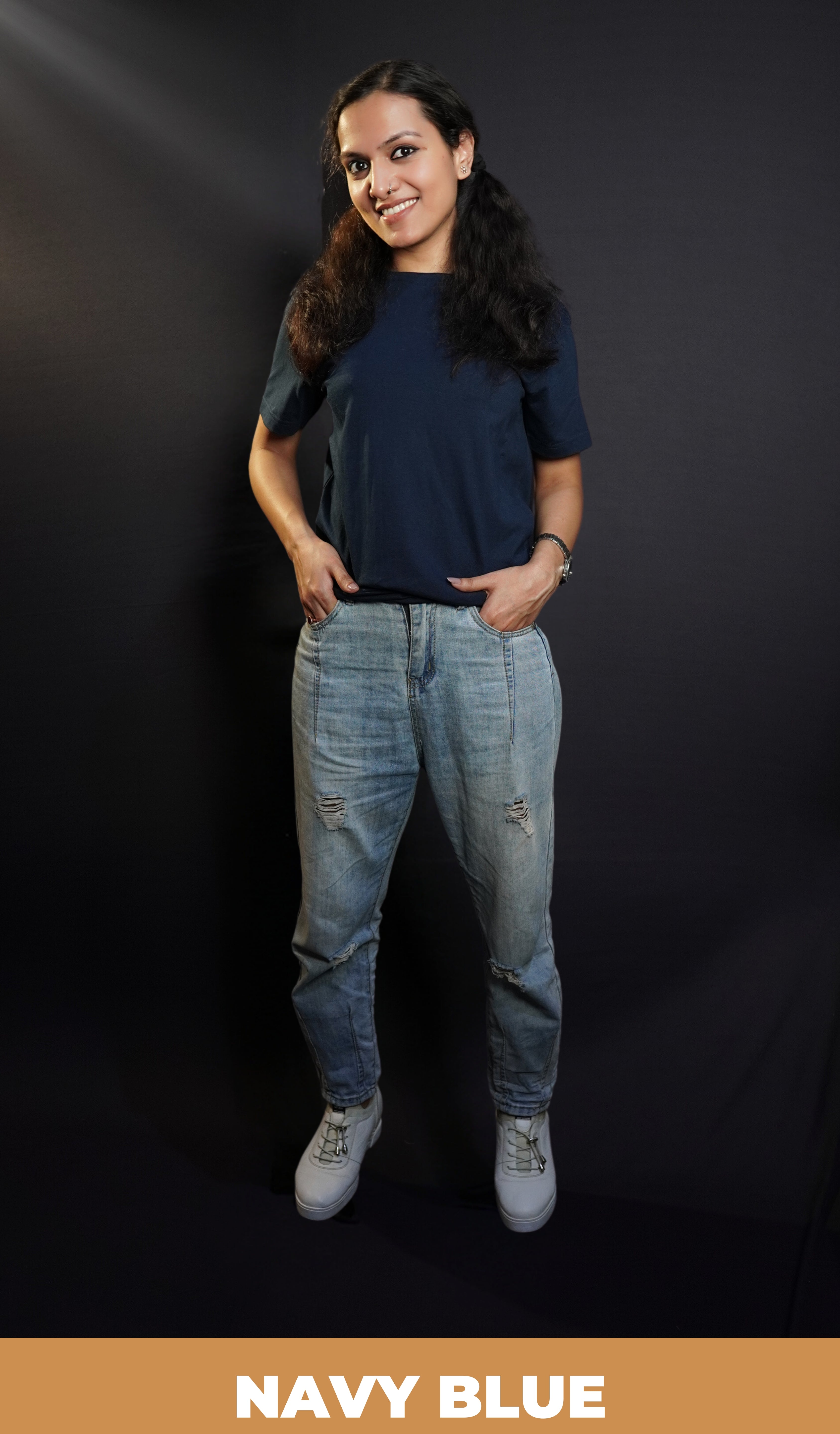 A woman wearing a men's summer short sleeved plain navy blue t-shirt, posing with her fingers inside the pockets of her jeans, highlighting a modish in vague fit-Muselot