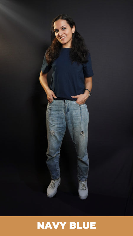 A woman wearing a men's summer short sleeved plain navy blue t-shirt, posing with her fingers inside the pockets of her jeans, highlighting a modish in vague fit-Muselot