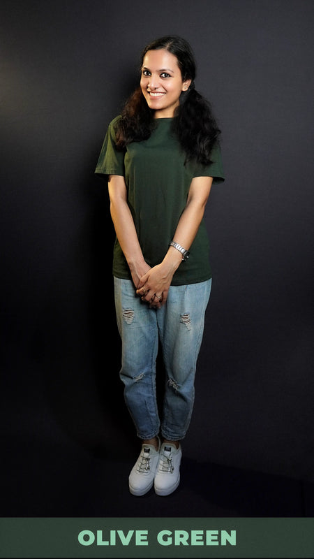 A model happily smiling standing against a dark background with her hand grabbing the other, wearing a moisture wicking stretchable plain cotton olive green t-shirt, highlighting a flowing aesthetic look-Muselot