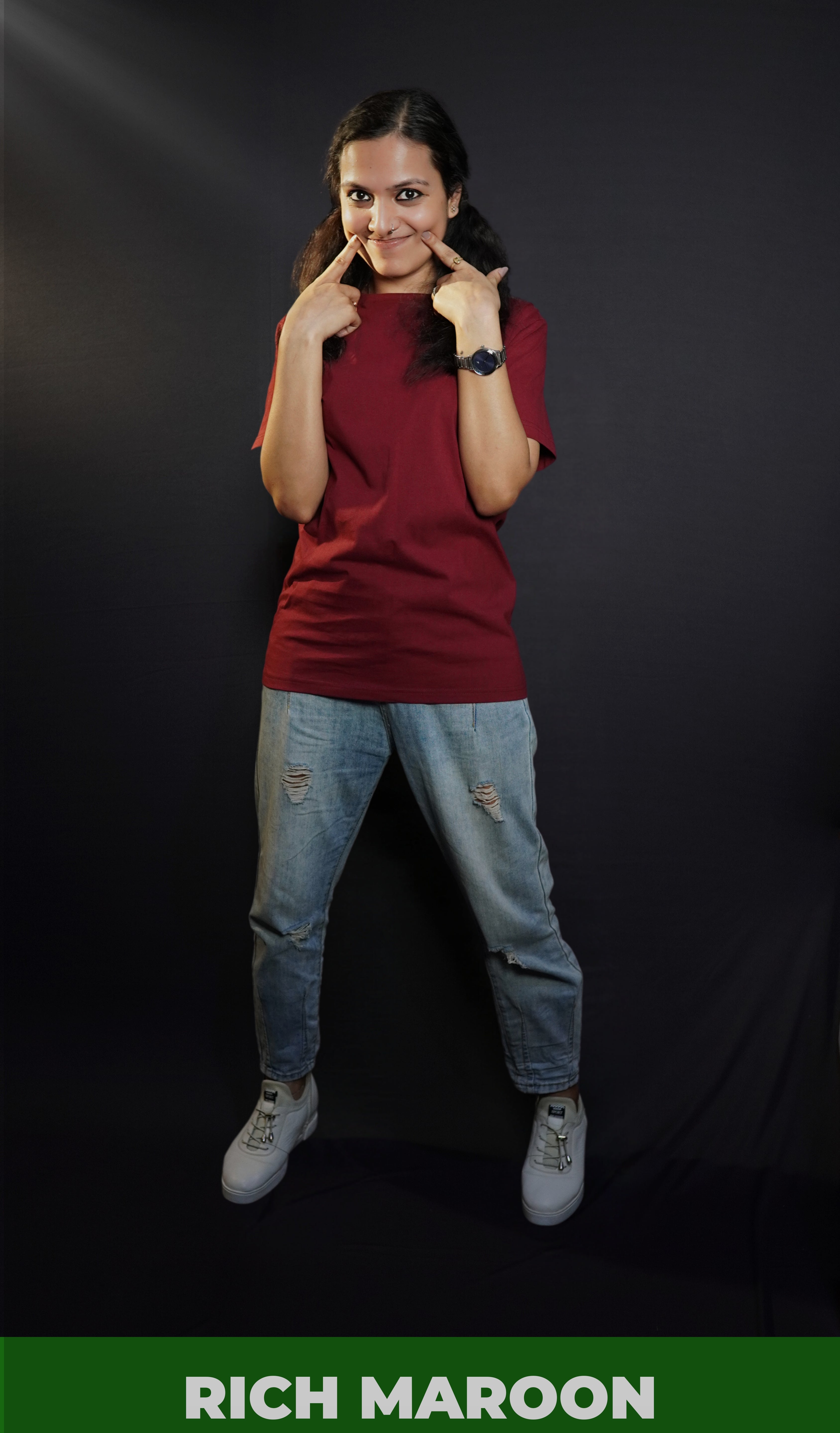 A woman smiling as her fingers poke into her cheeks, wearing a women's long length summer rich maroon t-shirt, showcasing a fashionable stylish look-Muselot