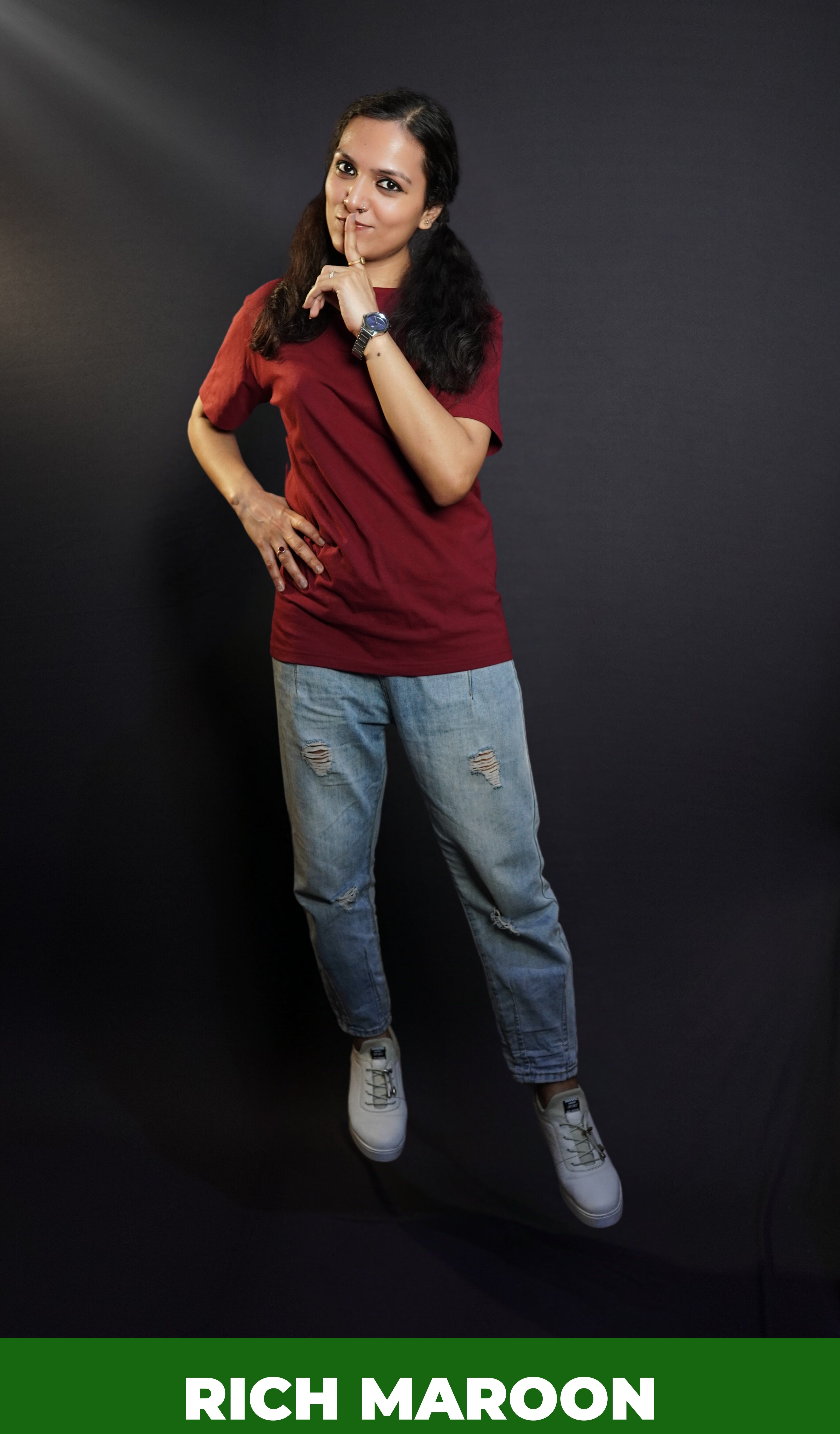 A woman wearing a round neck plain moisture wicking rich maroon t-shirt, posing with her finger on her lips and hand on her waist, highlighting a swank up to the minute look-Muselot