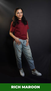 A woman wearing a short sleeved cotton stretchable rich maroon t-shirt, posing with her thumb inside the front pockets of her jeans, highlighting a stylish relaxed fit-Muselot