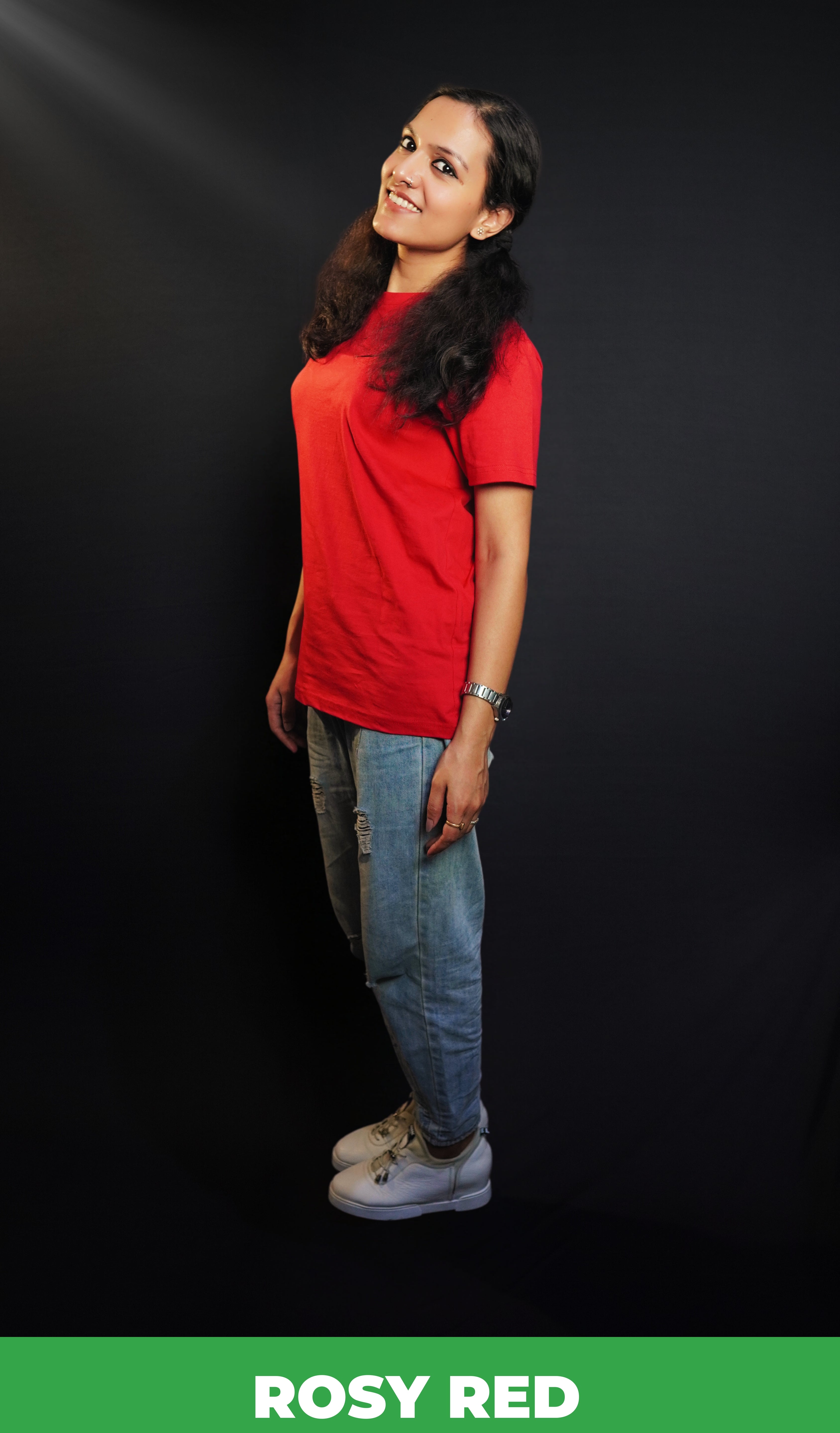 A woman standing sideways as her head bends slightly to the camera, smile on her lips, wearing a cotton round neck moisture wicking short sleeved rosy red t-shirt, highlighting a modish loose fit-Muselot