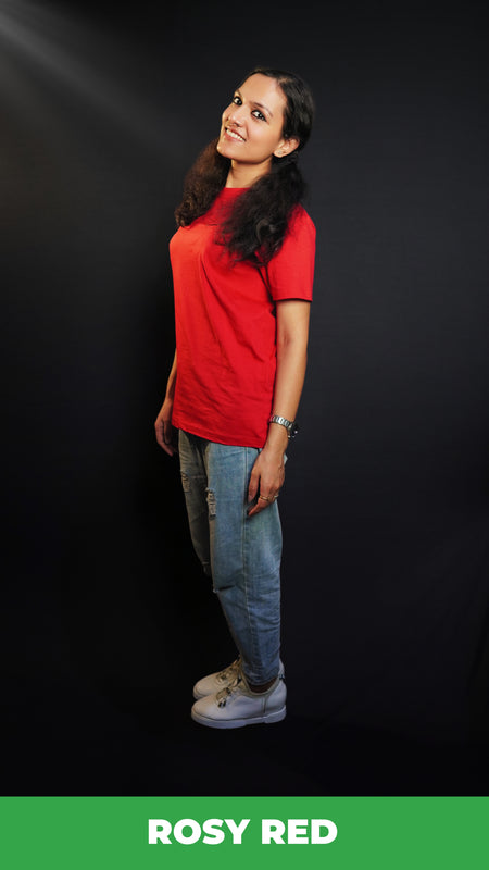 A woman standing sideways as her head bends slightly to the camera, smile on her lips, wearing a cotton round neck moisture wicking short sleeved rosy red t-shirt, highlighting a modish loose fit-Muselot