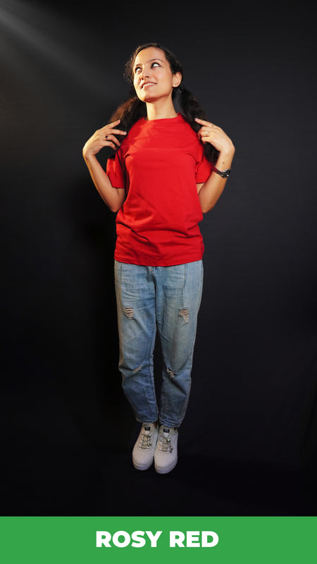 A model wearing a women's short sleeved long length rosy red t-shirt, posing with her hands grabbing sections of her hair as it lies on both of her shoulders, showcasing a modern laid back look-Muselot