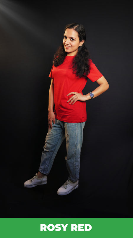 A woman wearing a long length short sleeved moisture wicking rosy red t-shirt, posing with her hands on her waist and other hanging on her side as she stand sideways against a dark background, highlighting a trendy in vogue look-Muselot