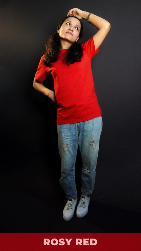 A woman wearing a unisex cotton long length stretchable rosy red t-shirt, posing with her hand on her head and other behind her waist looking sideways with her head up and bent slightly to her side, showcasing a trendy casual fit-Muselot