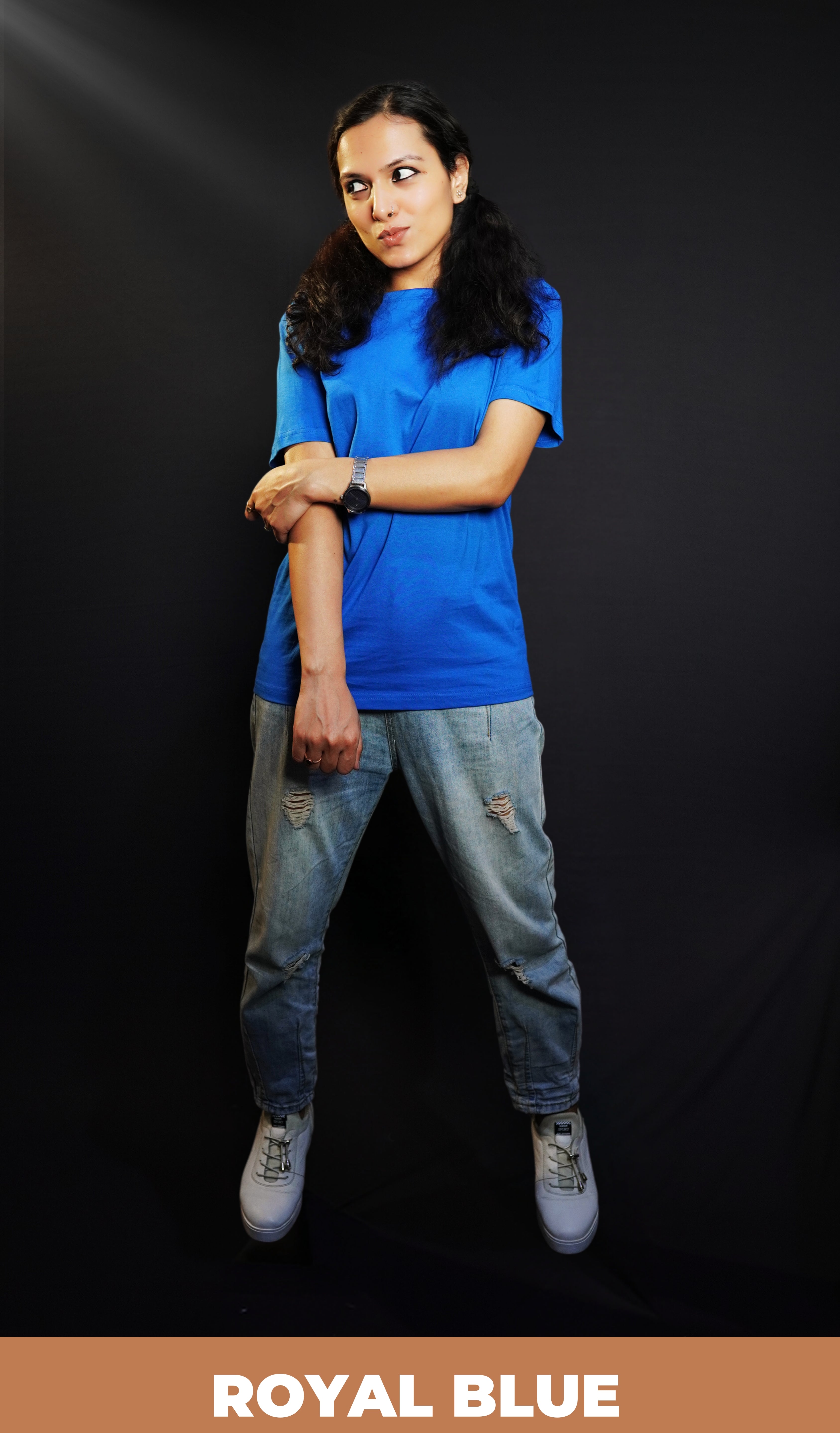 A woman wearing a stretchable round neck long length plain royal blue t-shirt, posing with her hand grabbing another that is hanging in front of her, pouting a little, highlighting a swank flowing fit-Muselot
