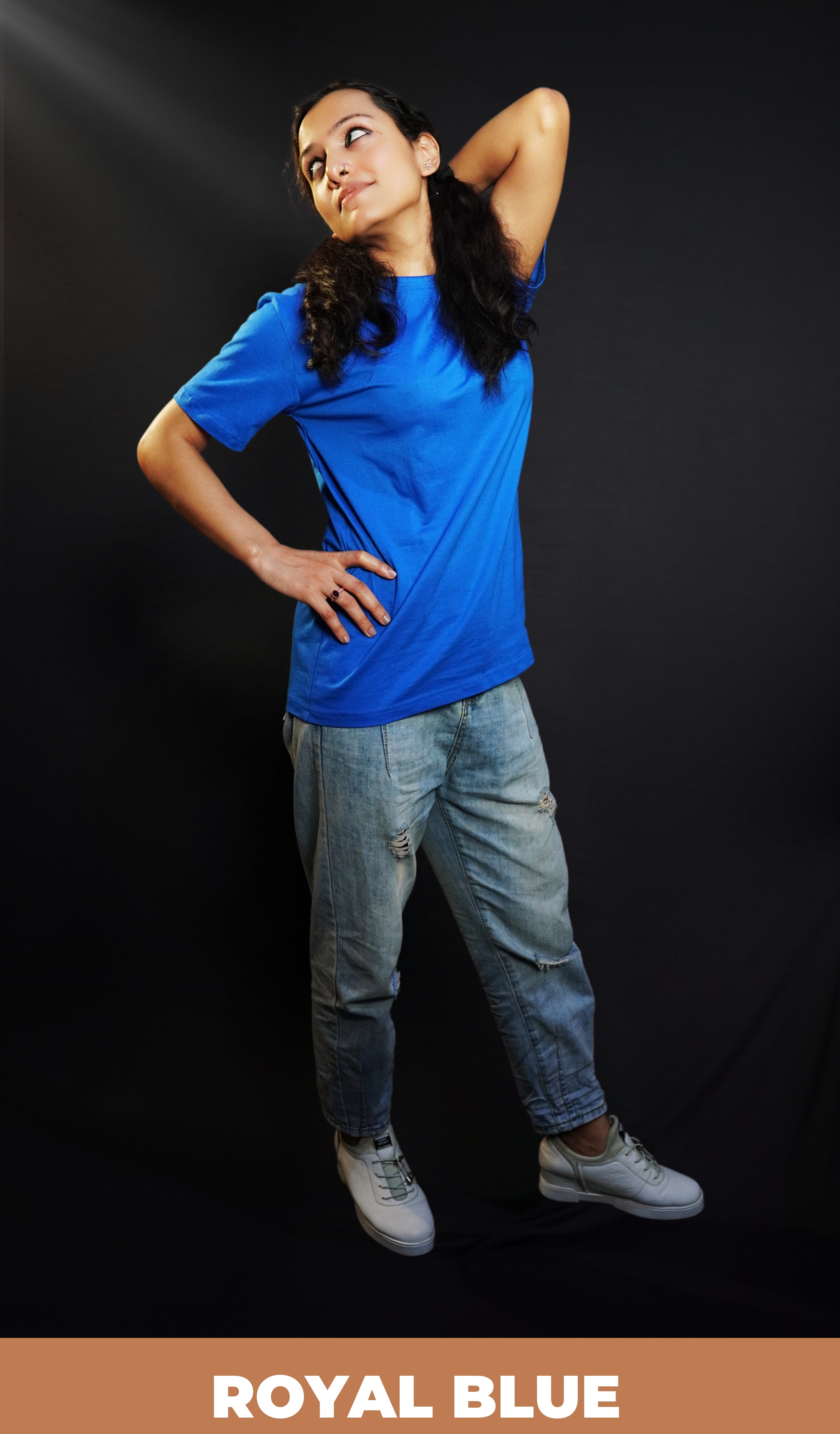 A stylish model wearing a long length adult's plain round neck royal blue t-shirt, posing with her hand up touching her back and another on her waist, showcasing an aesthetic cozy look-Muselot