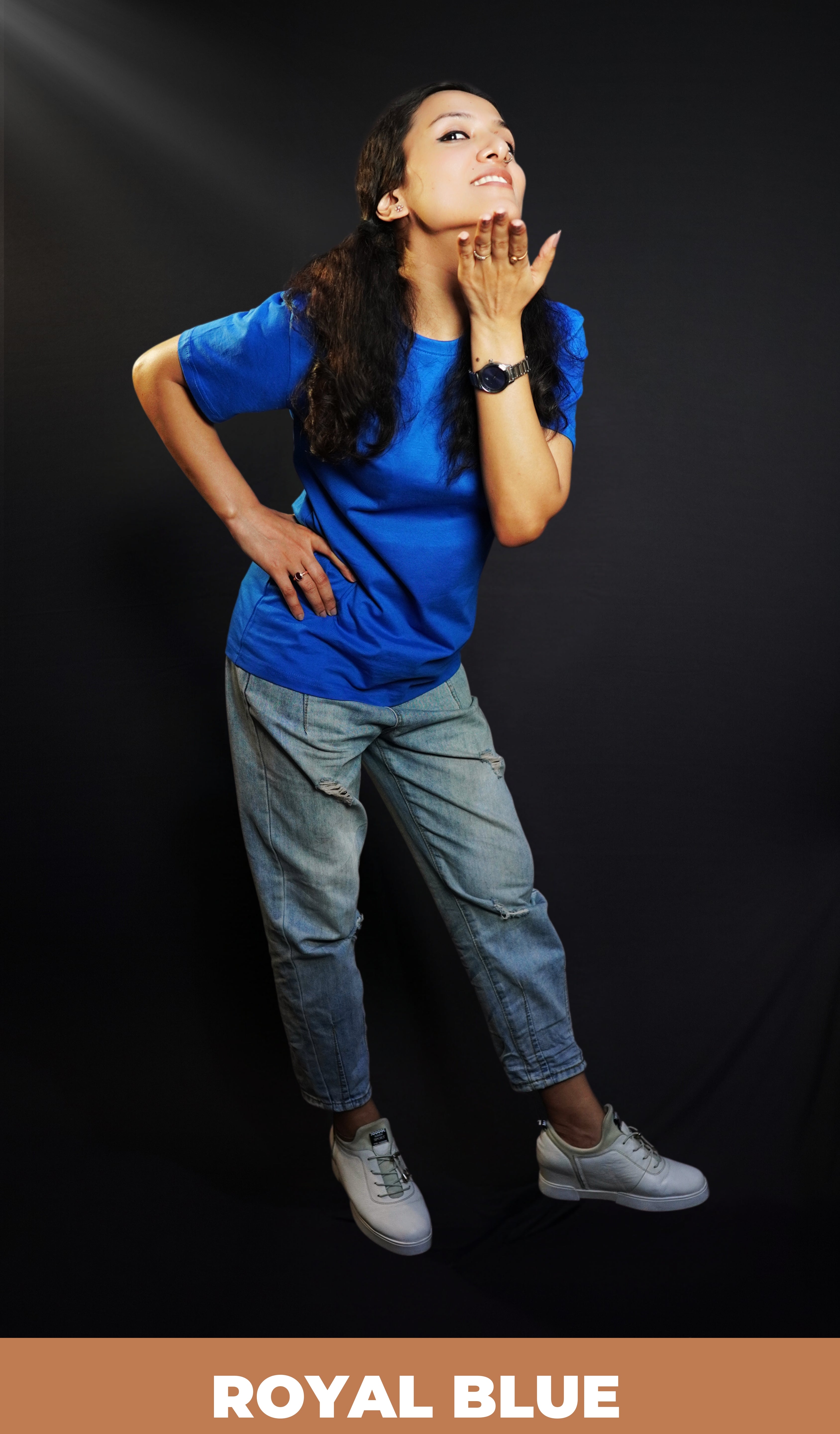 A pretty woman posing with her hand under her chin and other on her waist bending slightly forward, wearing a long length girl's moisture wicking royal blue t-shirt, highlighting a relaxed casual fit-Muselot
