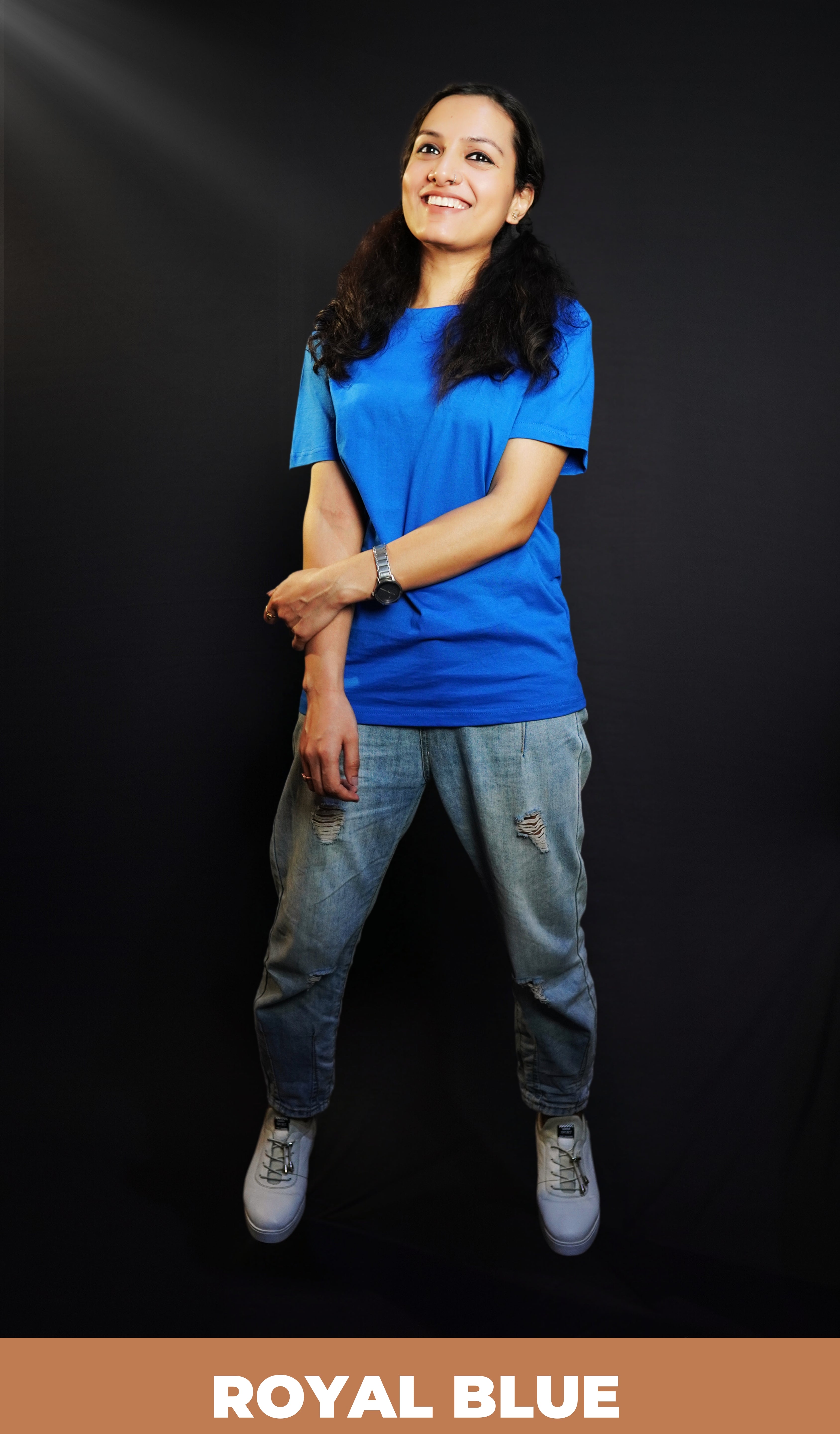 A woman smiling happily posing with her hand grabbing her forearm, wearing a long length royal blue plain round neck t-shirt, showcasing a popular easygoing fit-Muselot