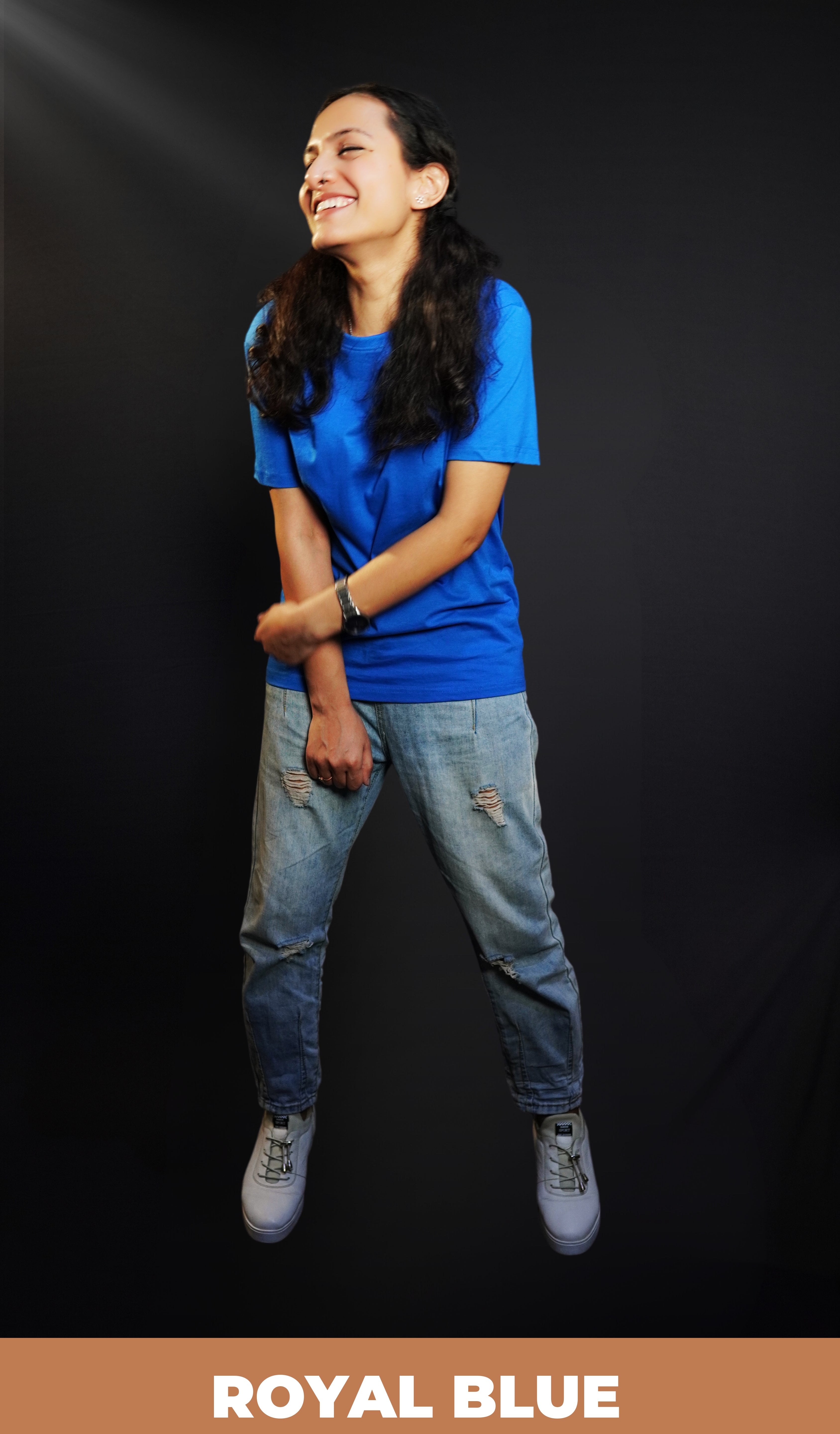 A woman laughing out loud with her hand grabbing her forearm standing against a dark background, wearing a long length cotton quick drying royal blue t-shirt, highlighting an in demand relaxed look-Muselot