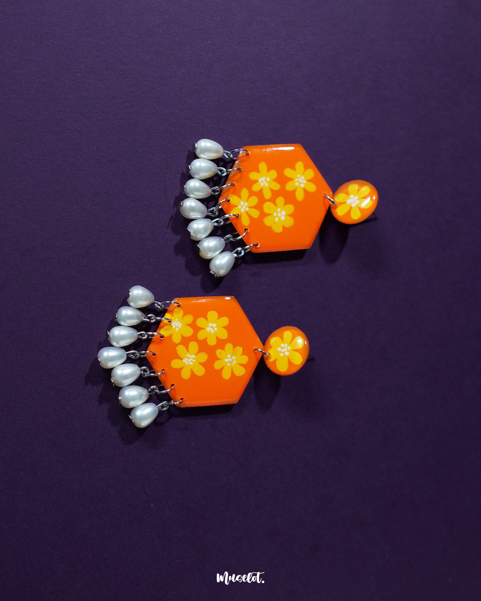 Top view of the Zafraan floral earrings, showing round orange studs with yellow flower motifs connected to hexagonal orange drops with matching floral designs, accented by dangling white pearl-like beads, highlighting their vibrant and detailed craftsmanship – Muselot.