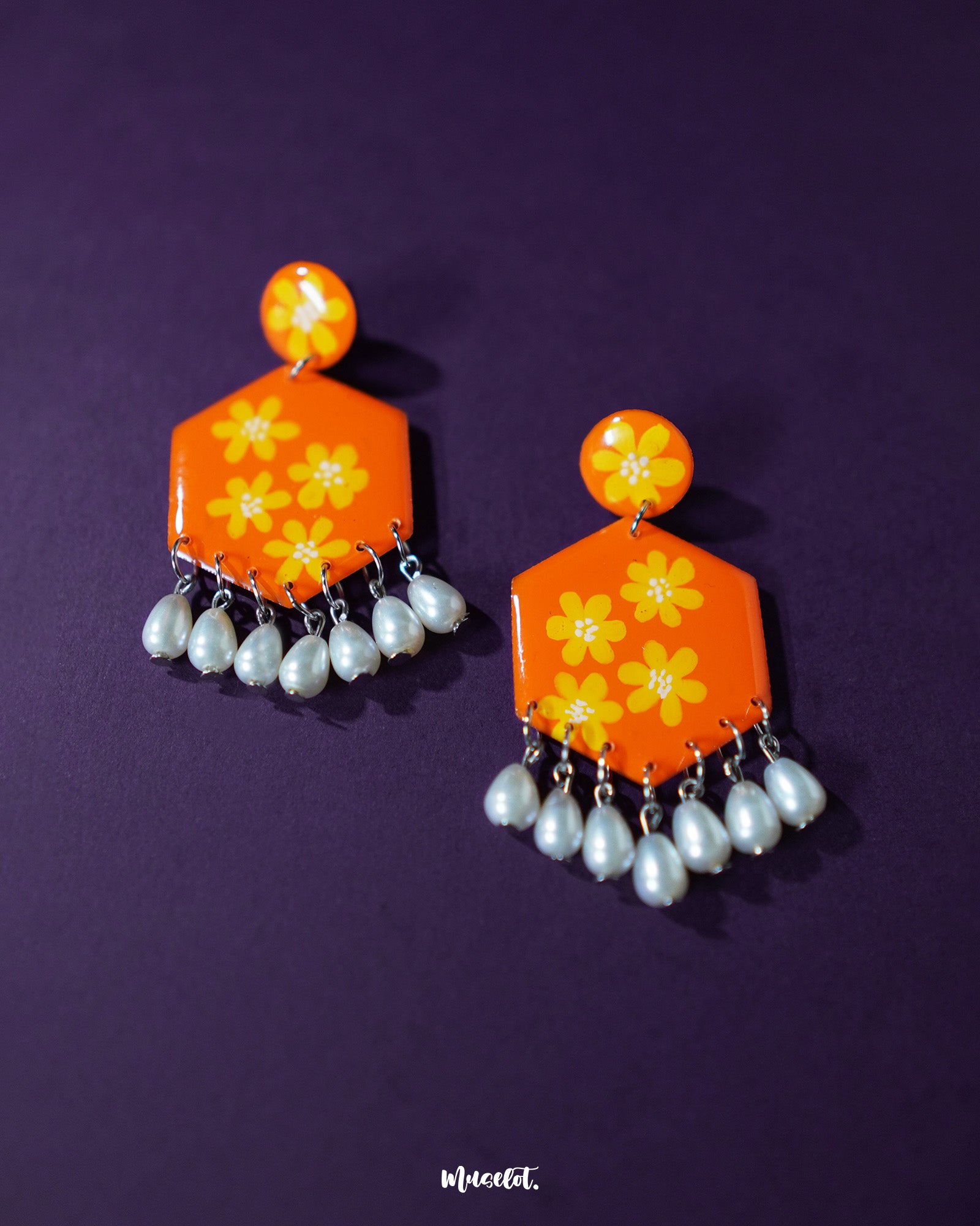 Zafraan floral earrings featuring round orange studs with yellow flower motifs attached to hexagonal orange drops decorated with matching floral designs, finished with dangling white pearl-like beads, elegantly showcased to emphasize their bright and cheerful design – Muselot.