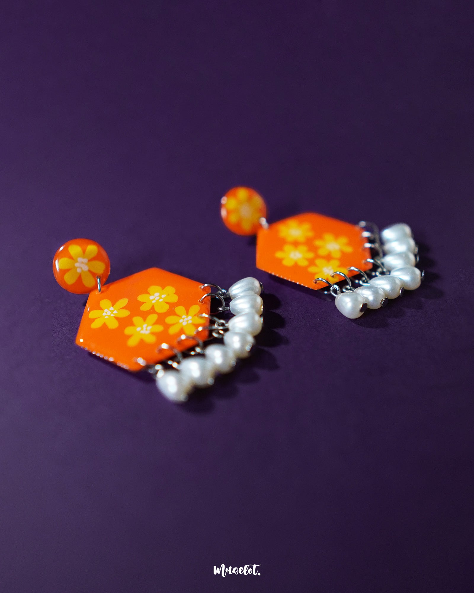 Side view of the Zafraan floral earrings, showcasing round orange studs with yellow flower motifs connected to hexagonal orange drops adorned with matching floral designs, finished with dangling white pearl-like beads, highlighting their intricate detailing and vibrant colors – Muselot.