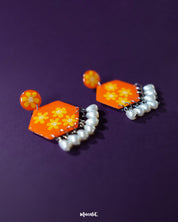 Side view of the Zafraan floral earrings, showcasing round orange studs with yellow flower motifs connected to hexagonal orange drops adorned with matching floral designs, finished with dangling white pearl-like beads, highlighting their intricate detailing and vibrant colors – Muselot.