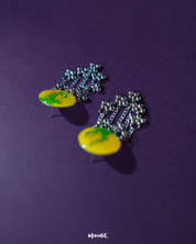 Close-up of Zarangi yellow drop earrings featuring circular tops with green brushstroke-style floral patterns, finished with cascading silver chains and metallic beads for a playful, ethnic charm — Muselot.