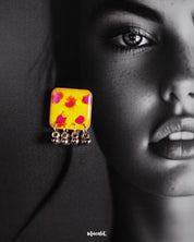 Close-up of model wearing Zard Bahaar earrings, showcasing yellow hand-painted square studs with pink-red floral accents and silver ghungroo drops – Muselot.