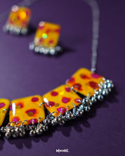 Zard Bahaar yellow floral jewelry set with hand-painted square tiles and silver ghungroo details, displayed against a purple background to highlight its vibrant traditional design – Muselot.