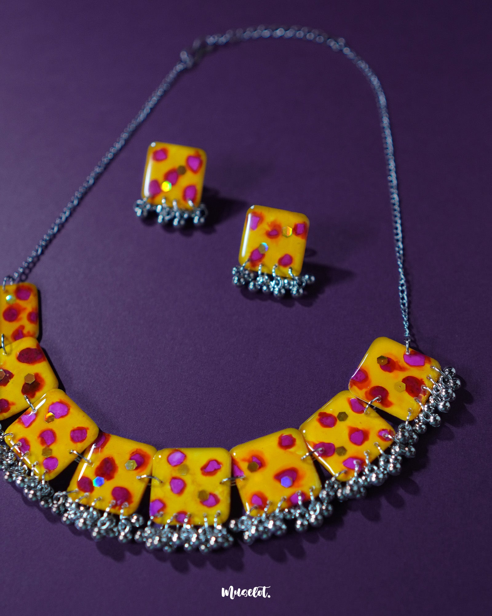 Angle shot of Zard Bahaar yellow floral jewelry set, featuring hand-painted necklace tiles with pink-red accents and matching earrings, displayed on a plain backdrop – Muselot.