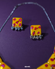 Front view of Zard Bahaar yellow floral jewelry set, showcasing hand-painted square pendants with pink-red accents and coordinated earrings with silver ghungroo details – Muselot.