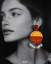 A closeup shot of a woman wears the Zardozi drop earrings, with warm mustard and rust-toned circular tops adorned in traditional hand-painted motifs and white pearl danglers—highlighting the rich craftsmanship and statement appeal of this artisanal pair — Muselot.