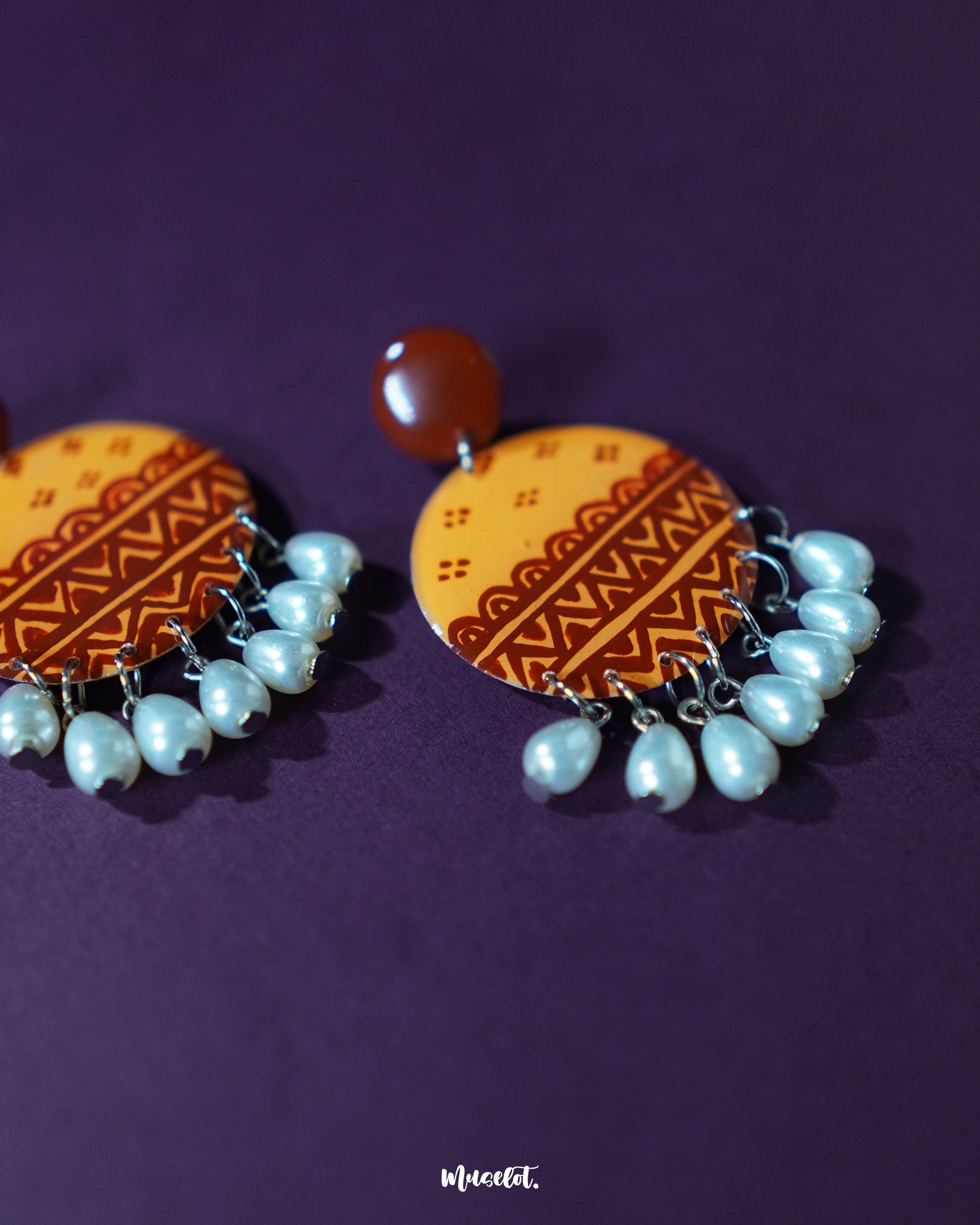 Close-up shot of Zardozi traditional handmade earrings with intricate mustard and rust patterns on a round base, adorned with delicate pearl-like drops, highlighting fine detailing and showcasing ethnic elegance — Muselot.