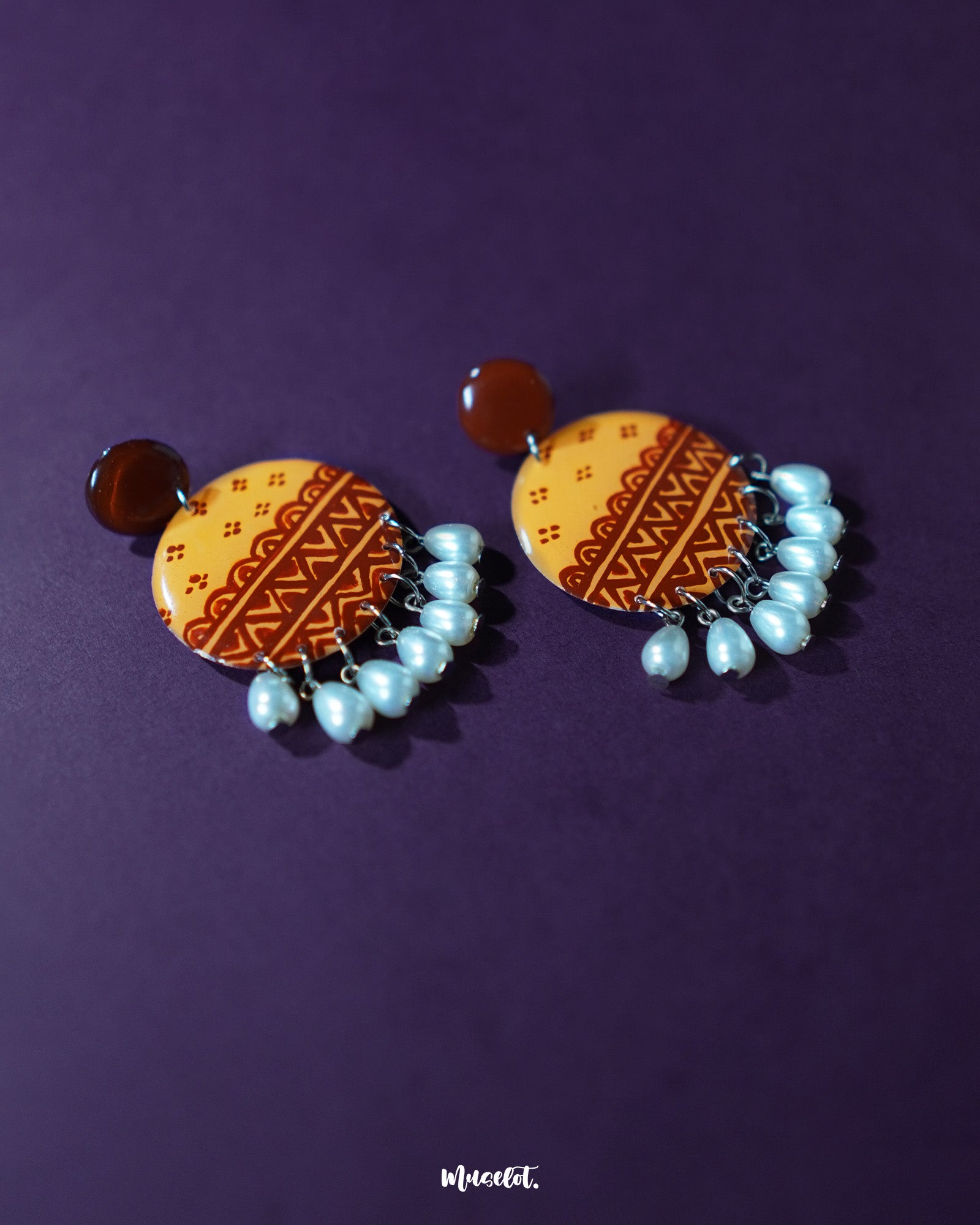 Zardozi traditional handmade earrings resting against a purple backdrop, featuring rich mustard embroidery with rust-toned floral accents and hanging white beads, showcasing intricate craftsmanship and highlighting cultural charm — Muselot.