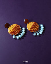 Zardozi traditional handmade earrings resting against a purple backdrop, featuring rich mustard embroidery with rust-toned floral accents and hanging white beads, showcasing intricate craftsmanship and highlighting cultural charm — Muselot.