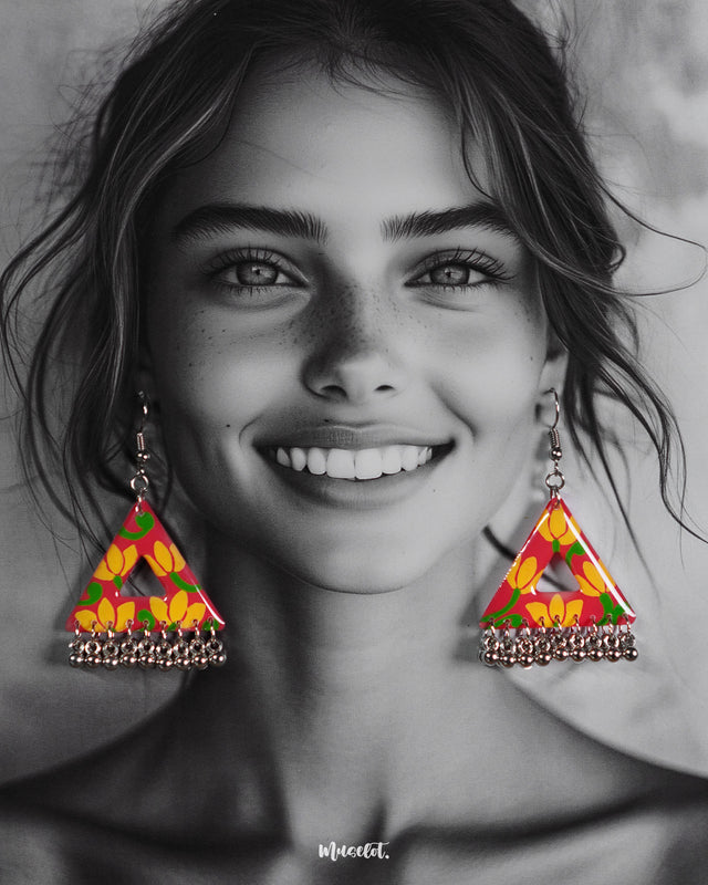 A model wearing the Zarmin floral triangle earrings, highlighting the bold hand-painted patterns in pink and yellow, and showcasing their playful silhouette with silver jhumki detailing that adds movement and charm, Muselot.