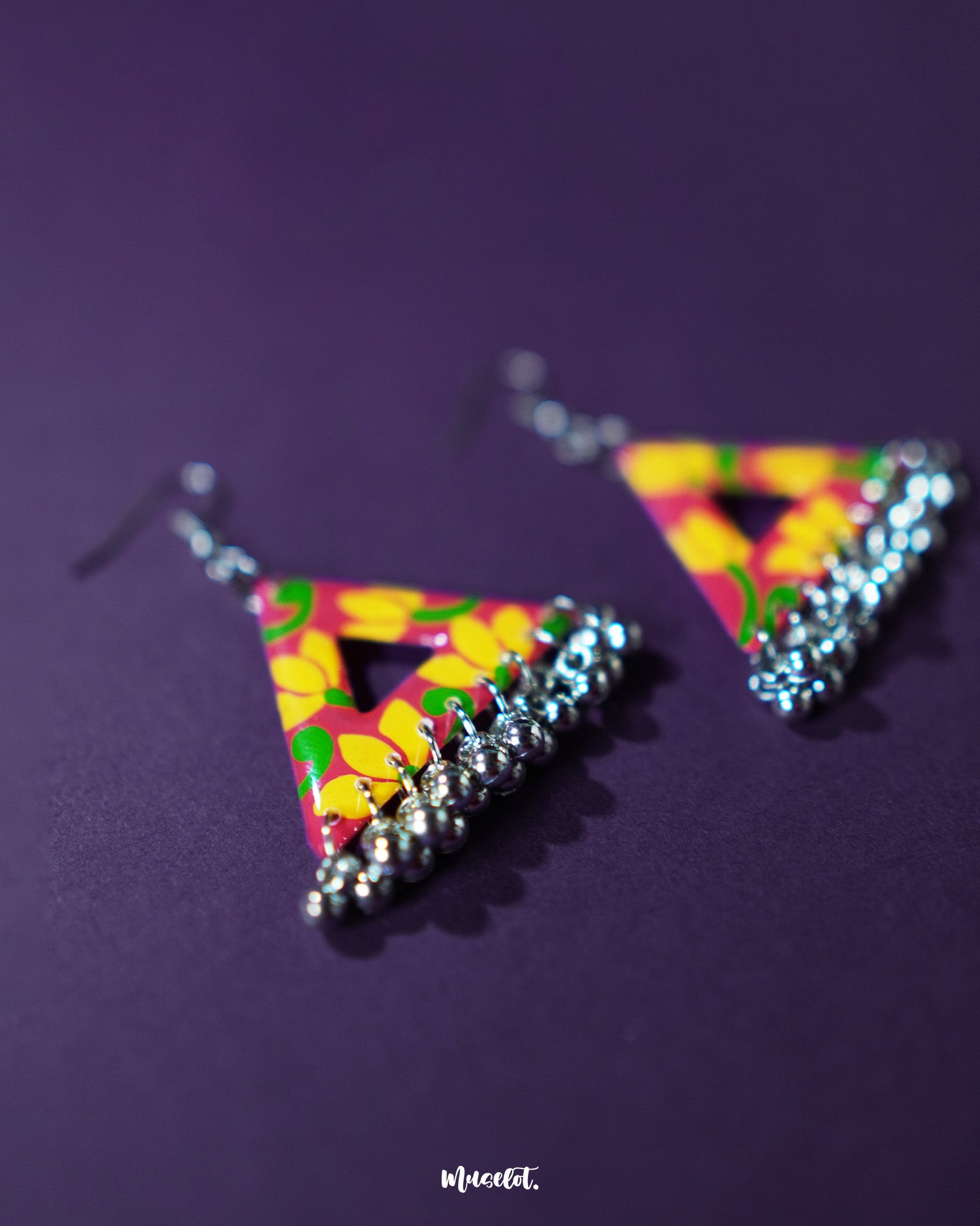 The Zarmin triangle floral earrings are a vibrant celebration of handcrafted artistry, highlighting bold yellow blooms on a red base and showcasing delicate silver jhumki drops that bring traditional charm to this modern geometric design — Muselot.