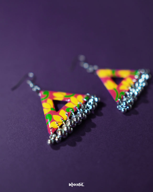 The Zarmin triangle floral earrings are a vibrant celebration of handcrafted artistry, highlighting bold yellow blooms on a red base and showcasing delicate silver jhumki drops that bring traditional charm to this modern geometric design — Muselot.