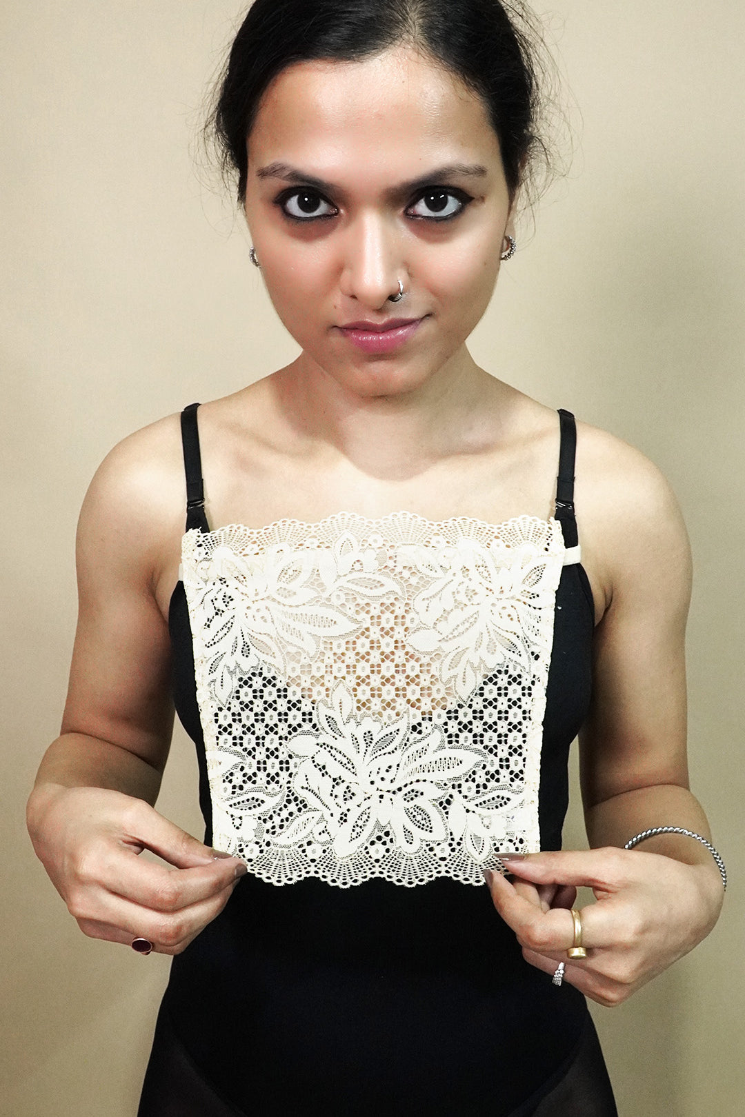 front view of woman holding beige lace camisole insert to show width and shape on beige background, showcasing lace mock camisole coverage for deep neckline tops – muselot