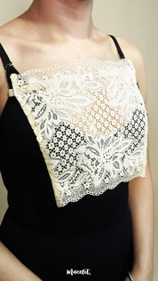 side close up of woman wearing beige lace camisole insert over black top on beige background, highlighting broad lace panel designed for better coverage on deep neck outfits – muselot