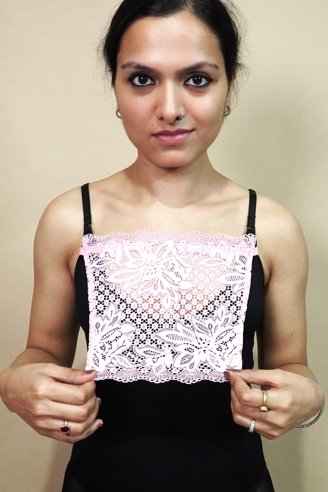 front view of woman holding baby pink lace camisole insert to display width and shape on beige background, showcasing lace mock camisole styling for covering deep neck tops – muselot