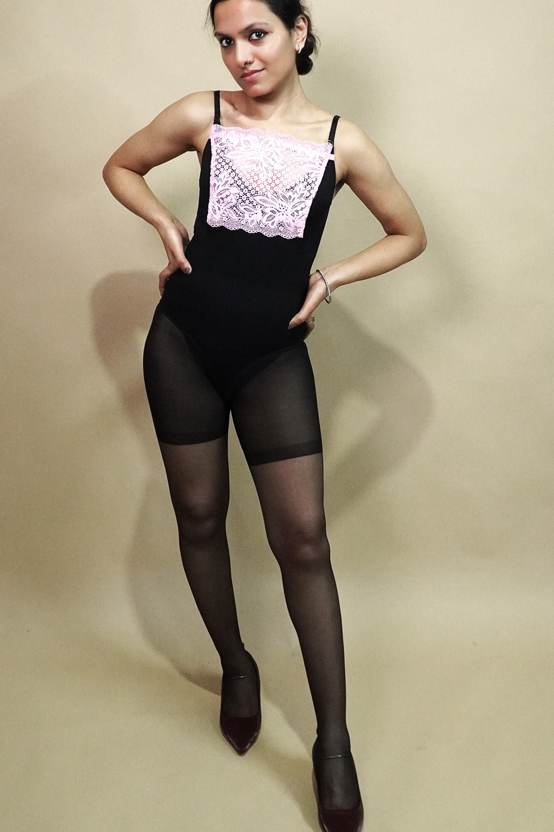 full body view of woman wearing baby pink lace camisole insert over black dress on beige background, showcasing neat neckline coverage with wide lace mock camisole for deep neck outfits – muselot