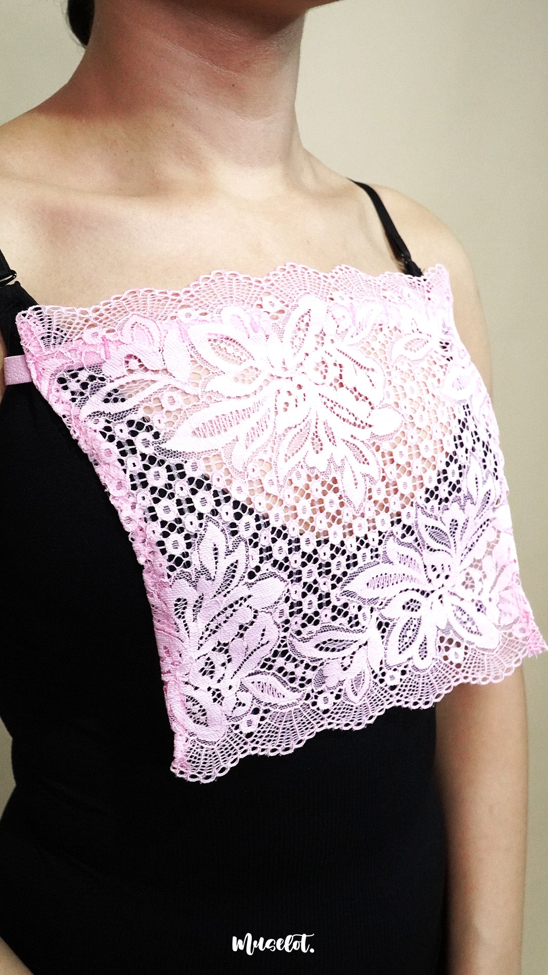 side angle close up of woman wearing baby pink lace camisole insert over black top on beige background, highlighting broad lace panel designed for better coverage on deep neckline styles – muselot