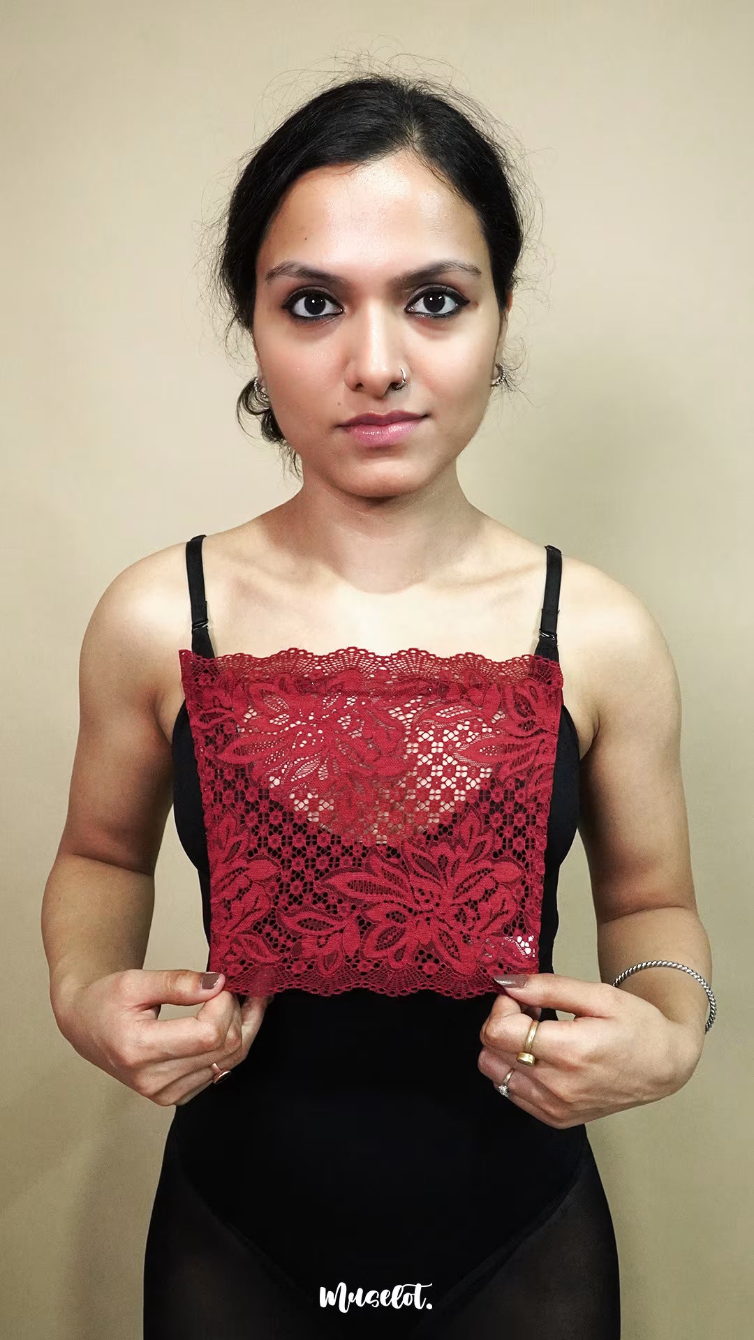 front view of woman holding maroon lace camisole insert to show width and neckline coverage on beige background, highlighting lace mock camisole styling for deep neck outfits – muselot