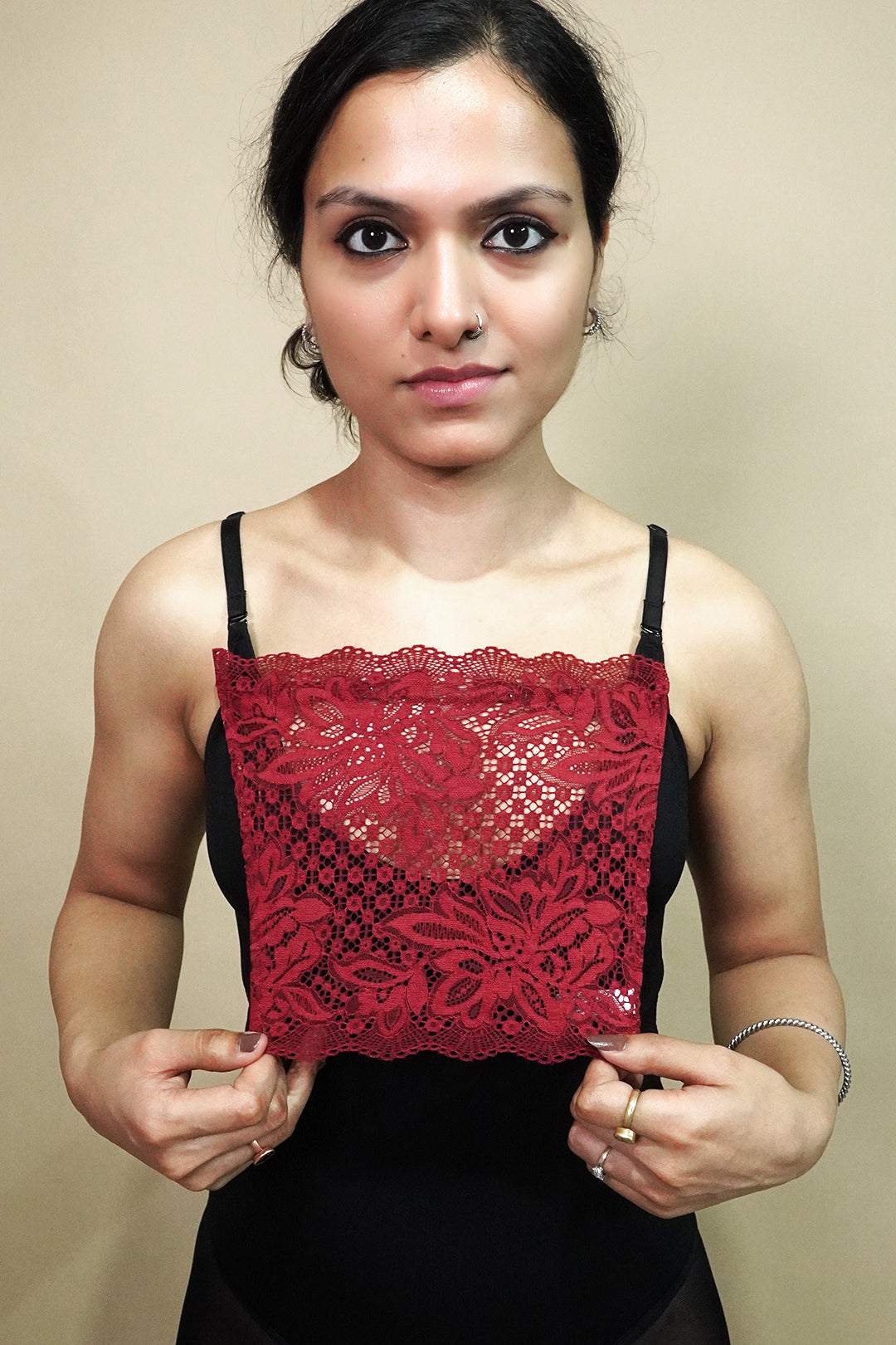 front view of woman holding maroon lace camisole insert to show width and neckline coverage on beige background, highlighting lace mock camisole styling for deep neck outfits – muselot