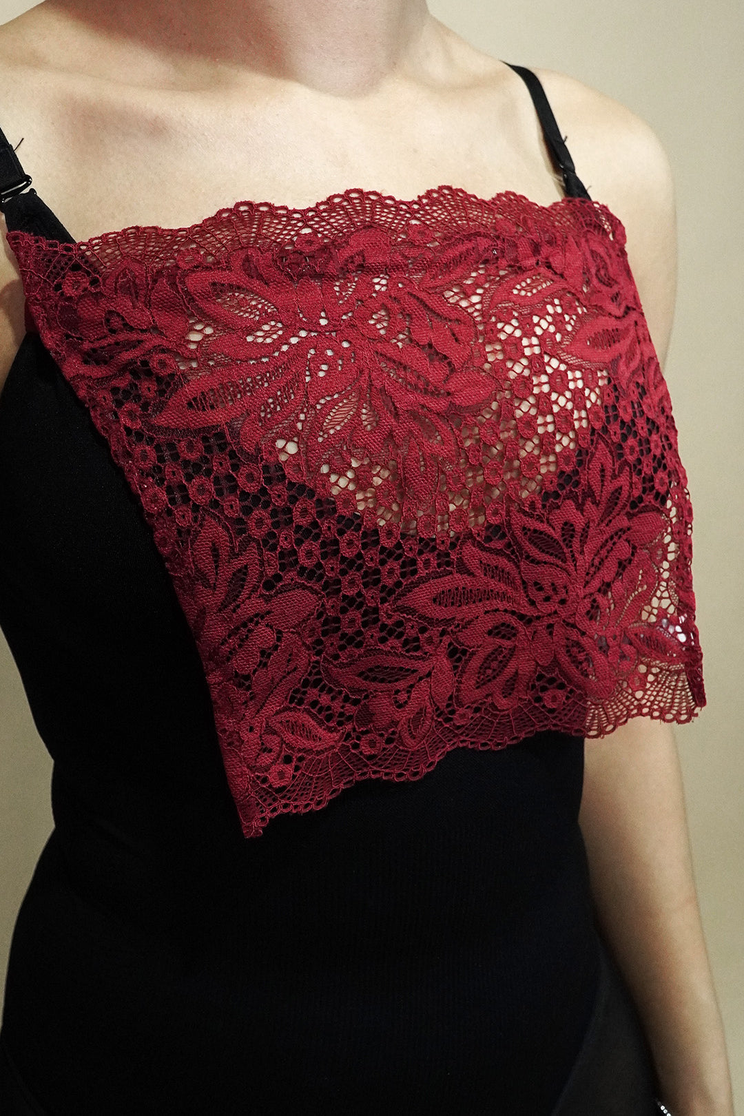 side angle close up of woman wearing maroon lace camisole insert over black top on beige background, highlighting wide lace coverage for low neckline dresses – muselot