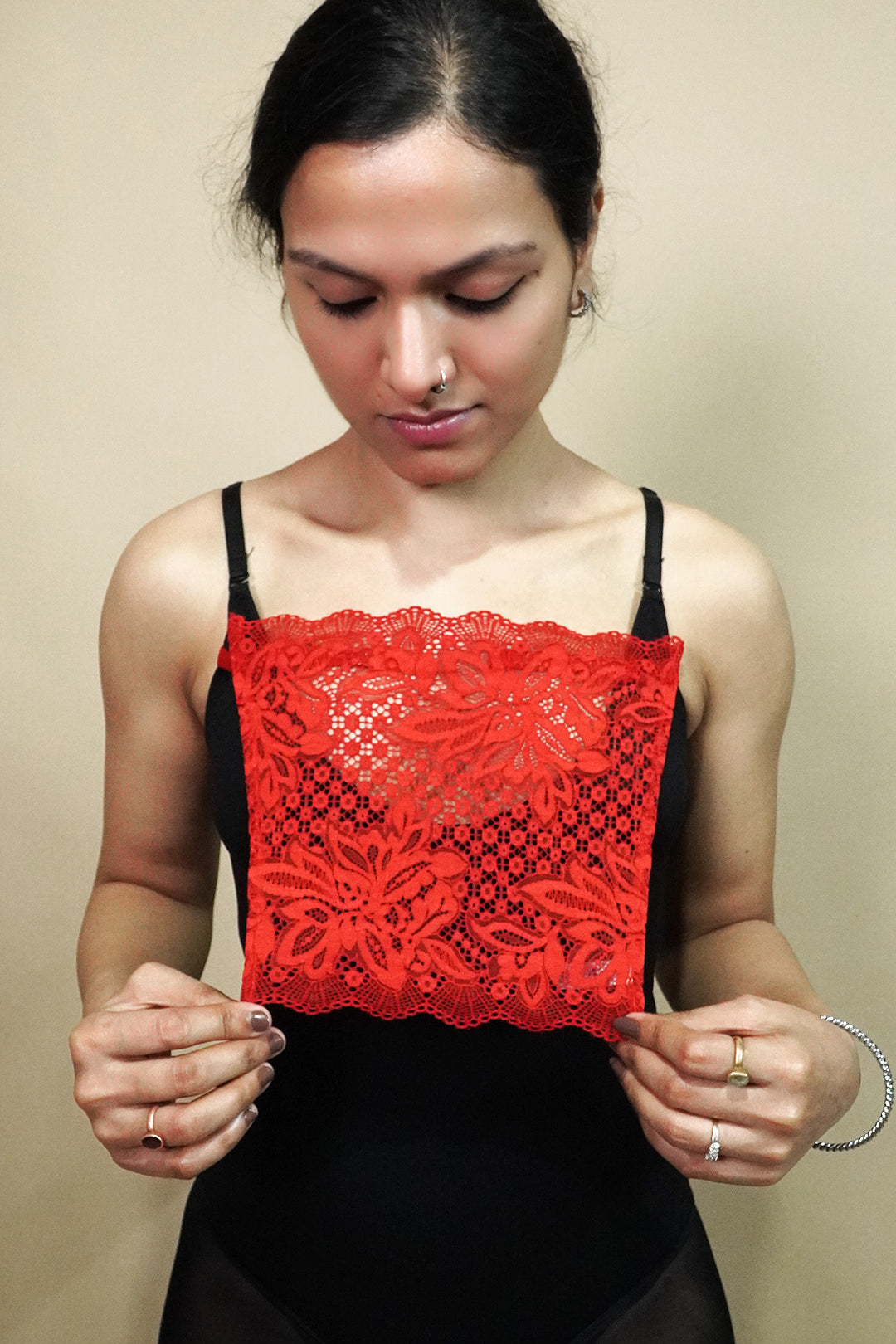 front view of woman holding red lace camisole insert to show width and coverage on beige background, highlighting lace mock camisole styling for deep neck tops – muselot