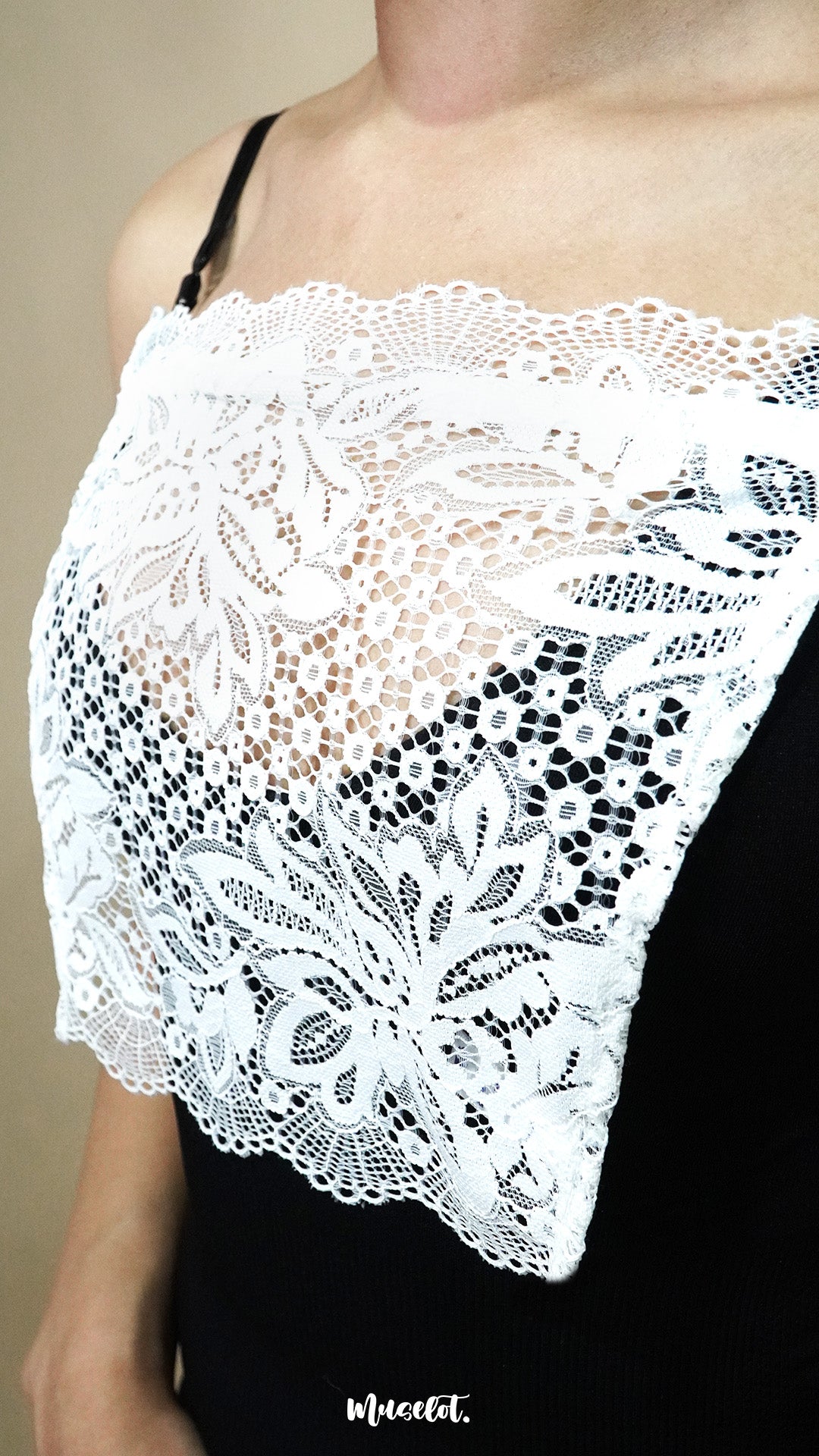 Side-angled close up of white lace camisole insert worn over black dress on beige background, showing broad lace design created to hide low necklines smoothly – muselot